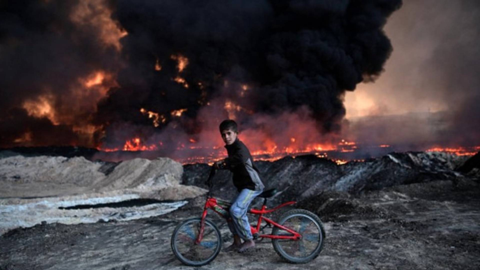 طفل عراقي يقود دراجته الهوائية وسط دخان النفط المشتعل