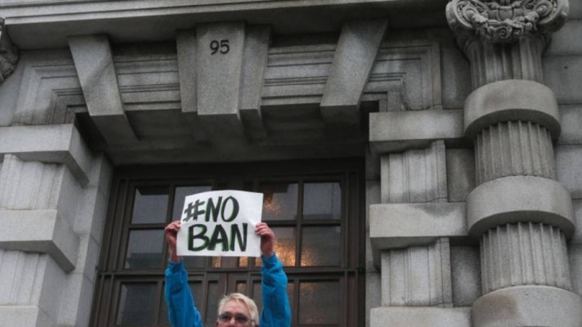  لافتة لأحد المحتجين أمام محكمة أميركية بوقف قرار ترامب