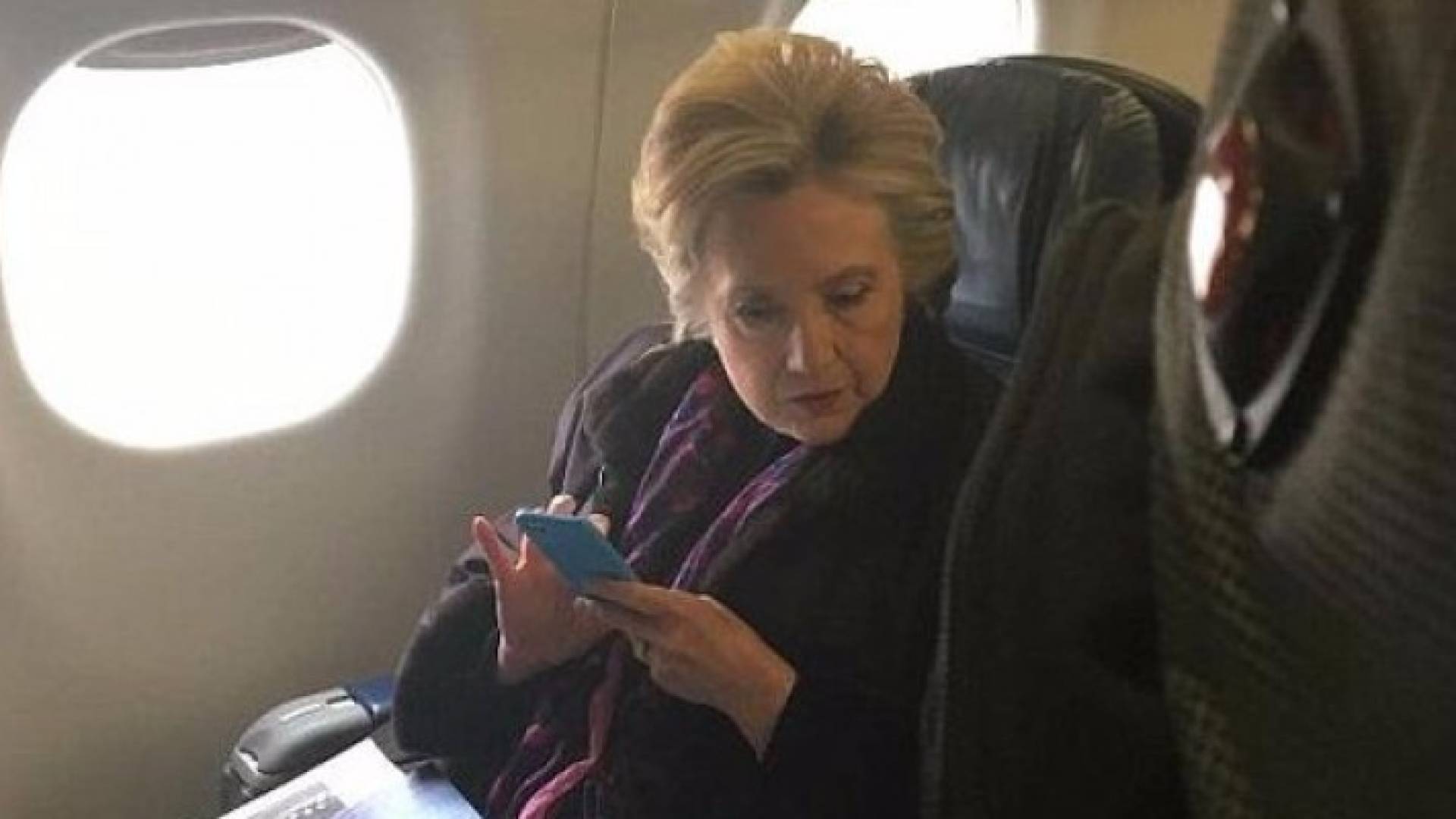 هيلاري_كلينتون وهي تقرأ في صحيفة بجوارها على الطائرة