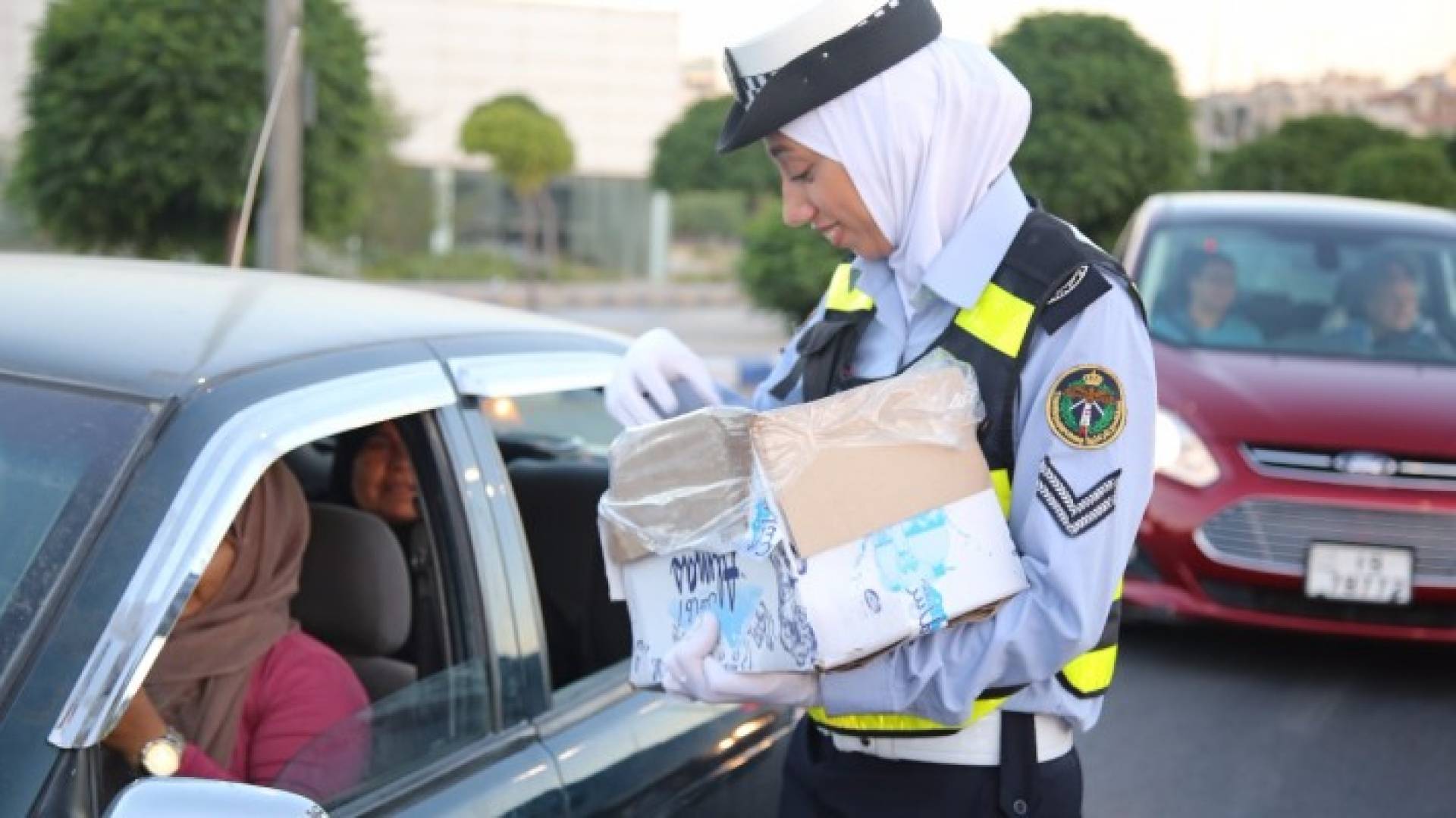 إحدى شرطيات السير وهي توزع الماء والتمر على سائقي المركبات