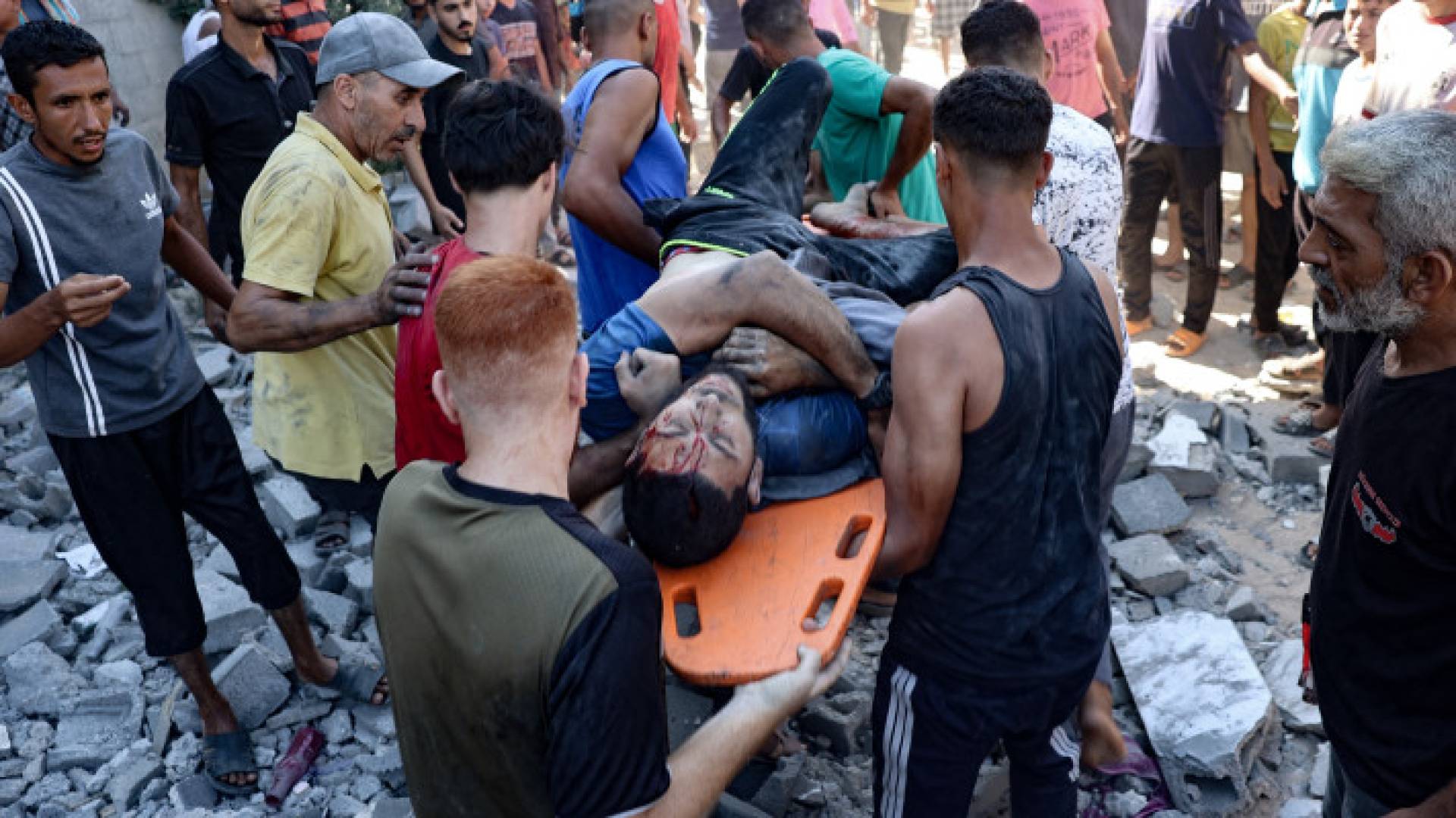 فلسطينيون يحملون شابا مصابا من مبنى قصفه الاحتلال في النصيرات بوسط قطاع غزة