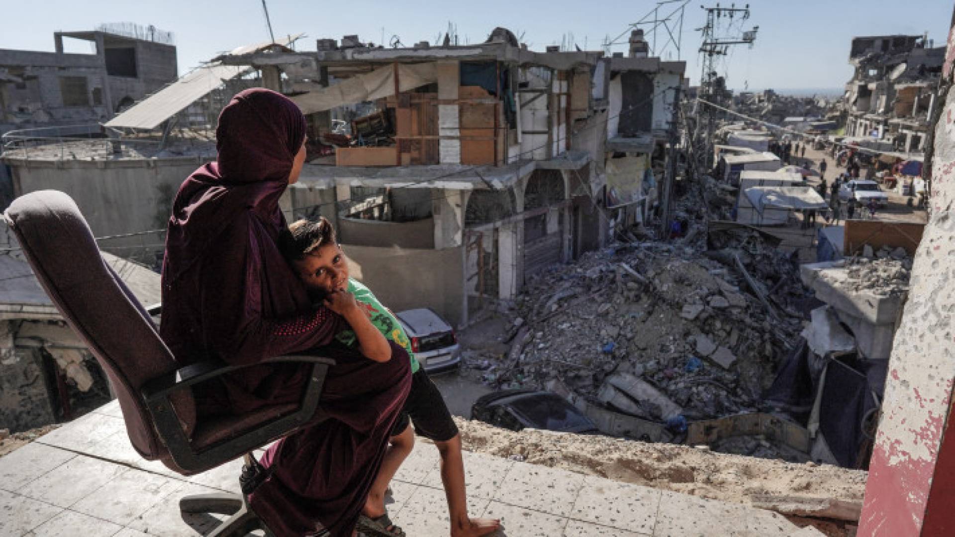 سيدة فلسطينية تجلس مع ابنها على شرفة منزلها الذي دمر بعدوان الاحتلال جنوب غزة