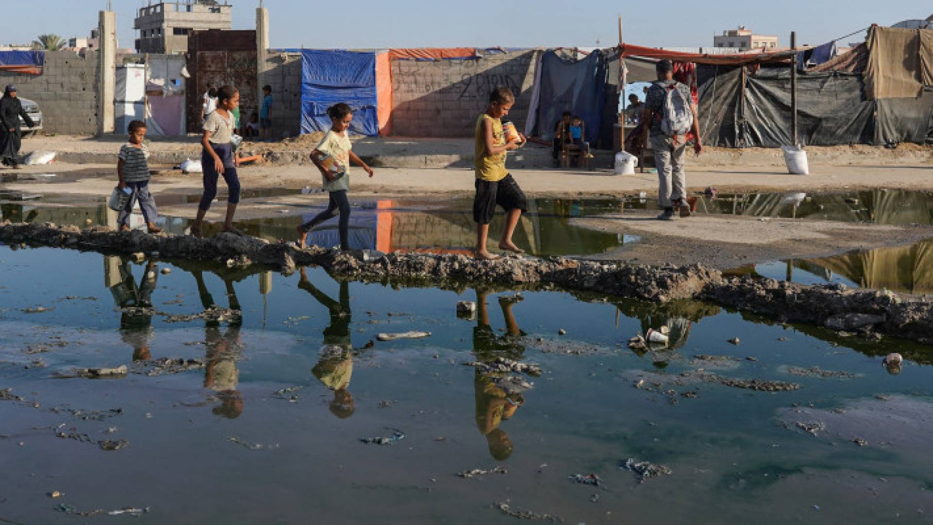 أطفال يمشون بالقرب من مياه الصرف الصحي الراكدة في دير البلح وسط غزة