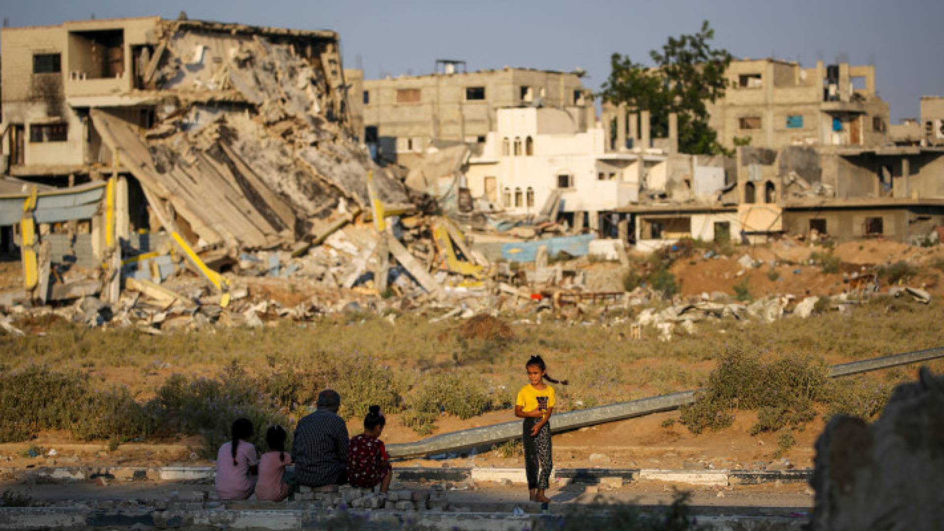 أشخاص يجلسون بالقرب من أنقاض المباني التي دمرت خلال قصف الاحتلال على مخيم المغازي للاجئين الفلسطينيين