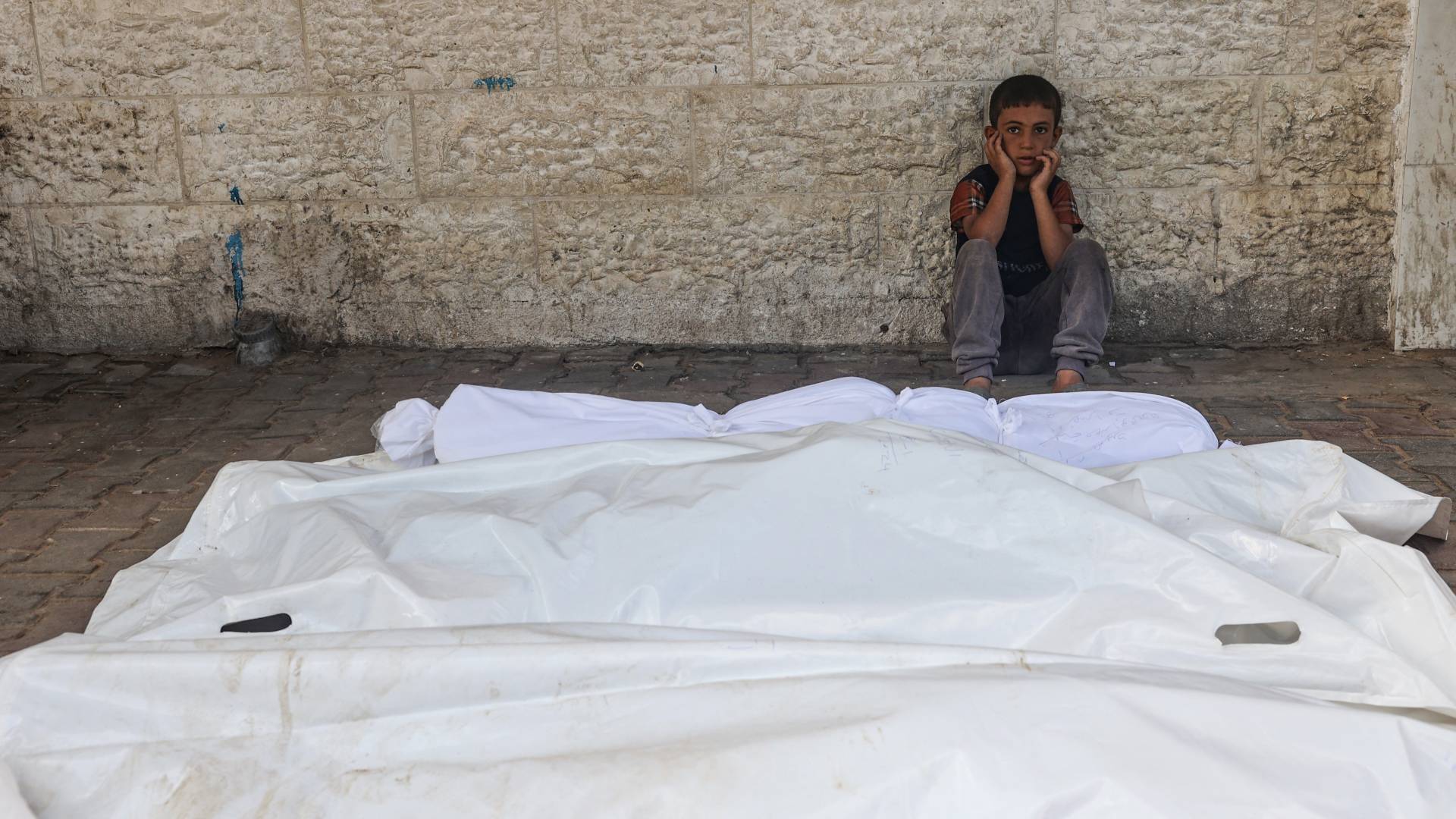 طفل فلسطيني يجلس بالقرب من جثامين الشهداء في غزة