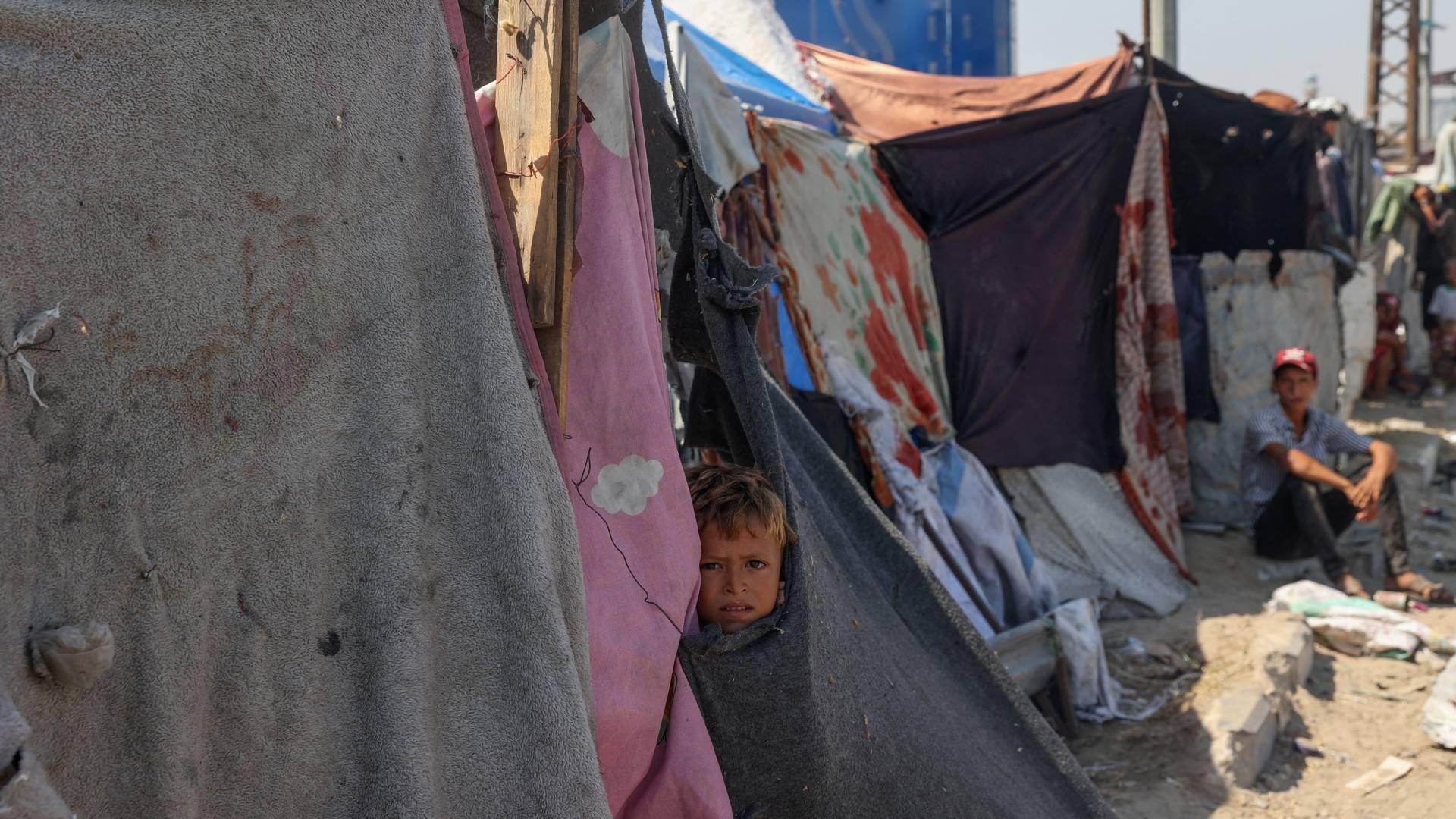 نازحون فلسطينيون يجلسون بجوار خيامهم في مخيم مؤقت للنازحين أقيم على جانب الطريق في دير البلح وسط قطاع غزة