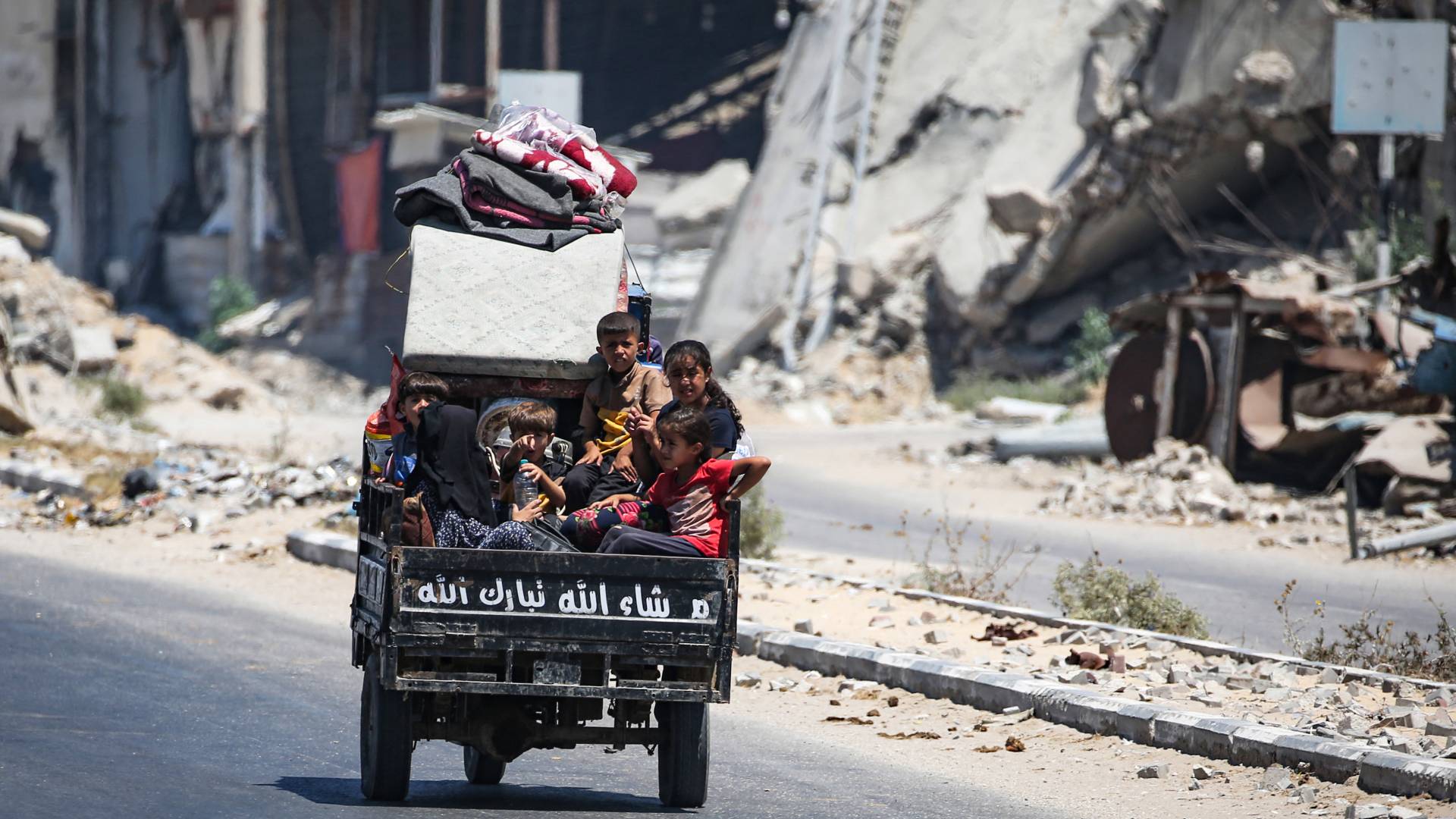 أطفال يجلسون في الجزء الخلفي من مركبة صغيرة وسط الدمار الذي خلفه الاحتلال دير البلح