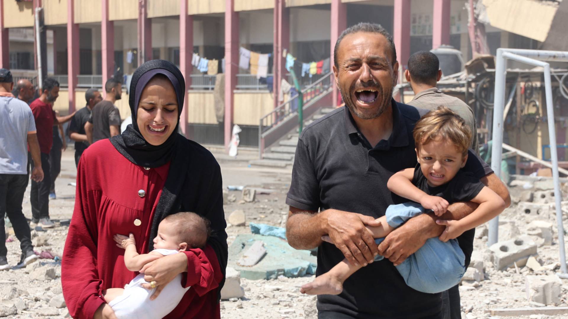 فلسطينيان يحملان طفليهما عقب غارة على مدرسة تؤوي نازحين في وسط غزة