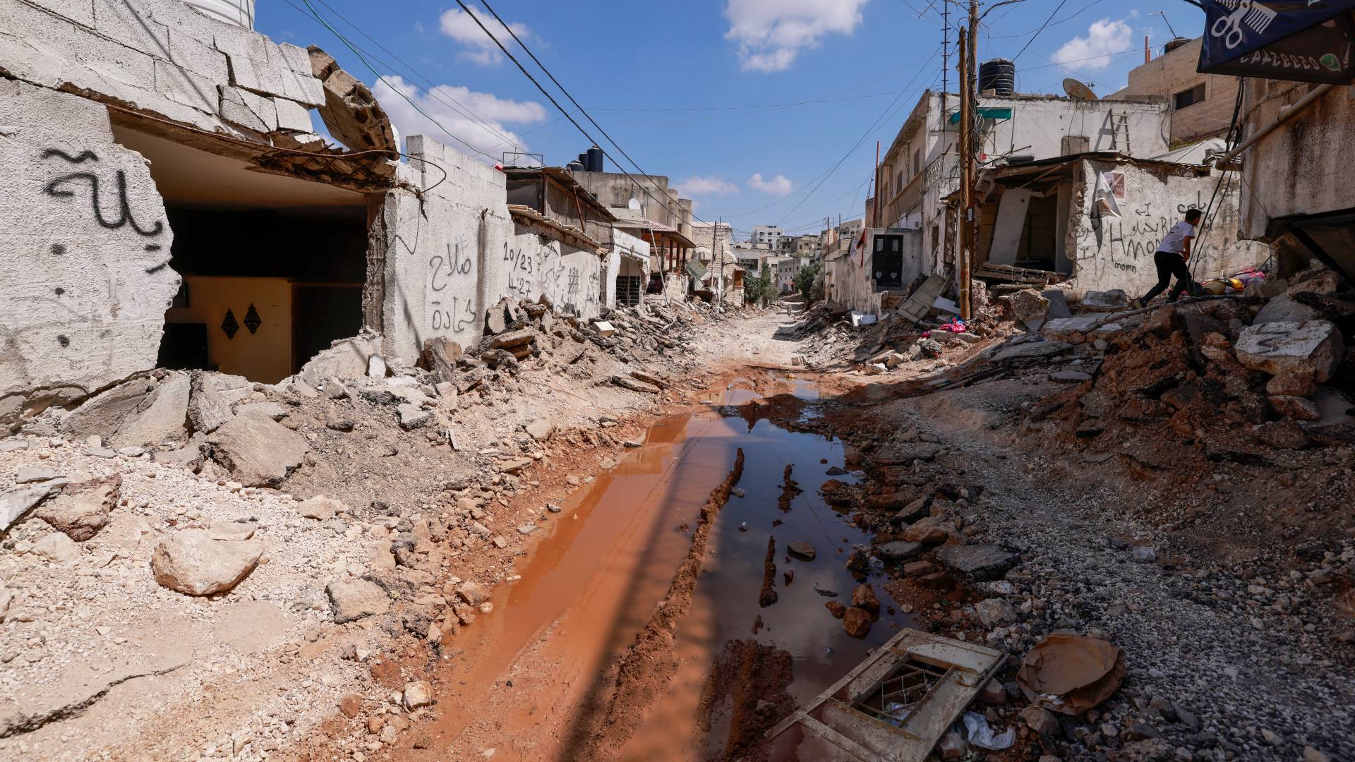 فلسطينيون يتفقدون الأضرار المحيطة بشارع دمرته الجرافات بعد غارة للاحتلال في الحي الشرقي لمدينة جنين