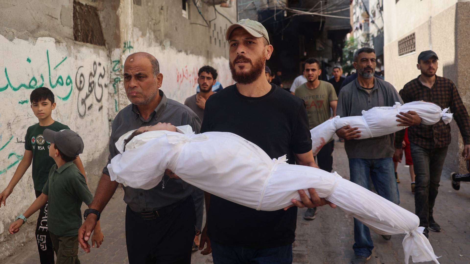 فلسطينيان يحملون جثامين شهداء في مخيم النصيرات وسط قطاع غزة