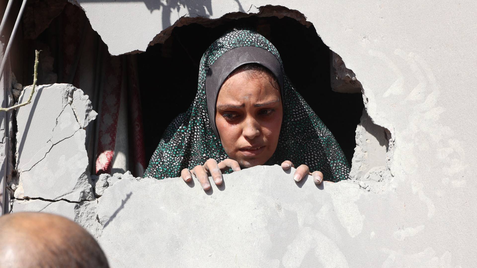 فلسطينية تسترق الأنظار بحزن من خلف جدار اخرقته قنابل الاحتلال "أ ف ب"