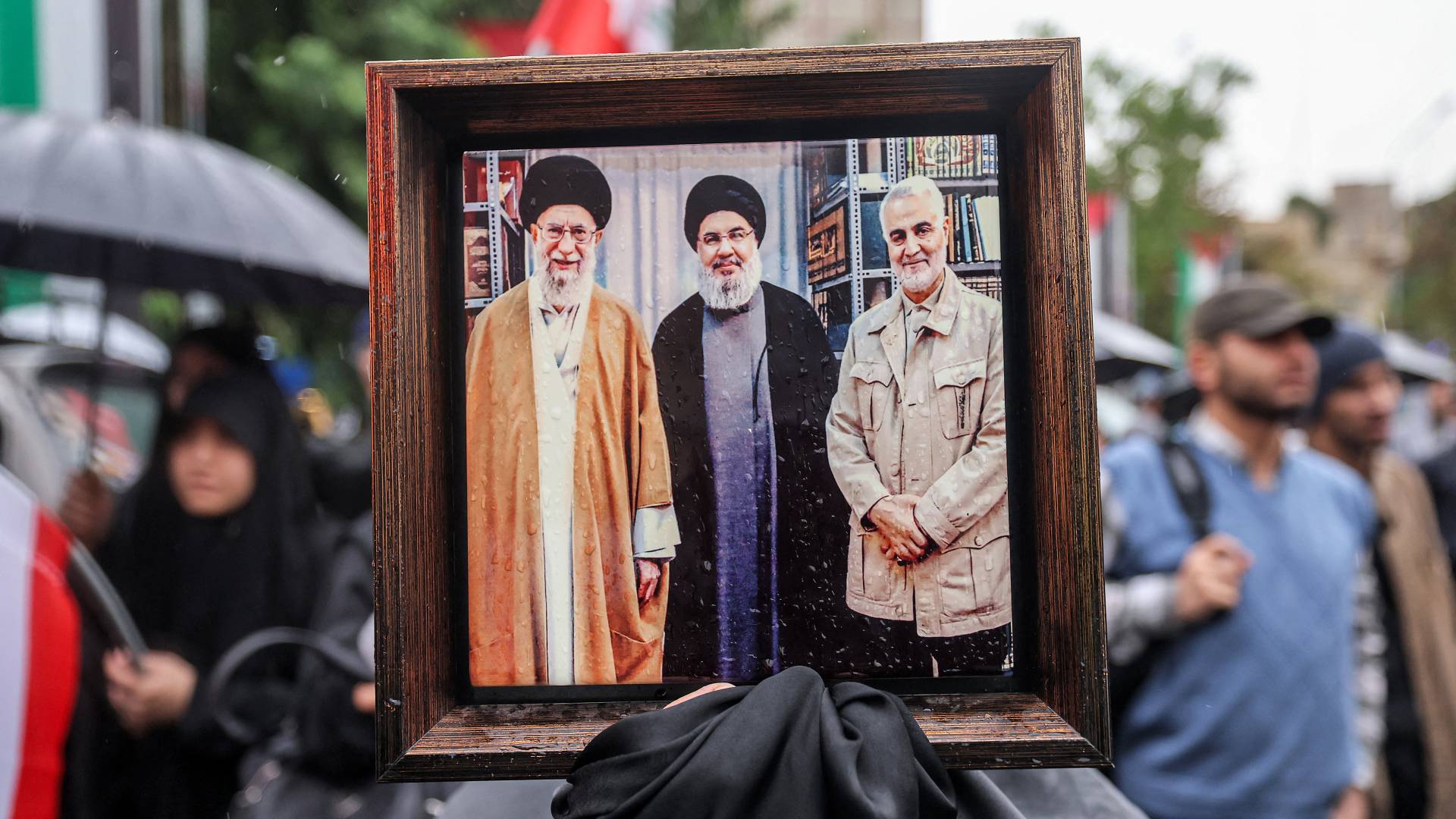 متظاهر يحمل صورة للمرشد الأعلى الإيراني علي خامنئي وحسن نصر الله وقاسم سليماني