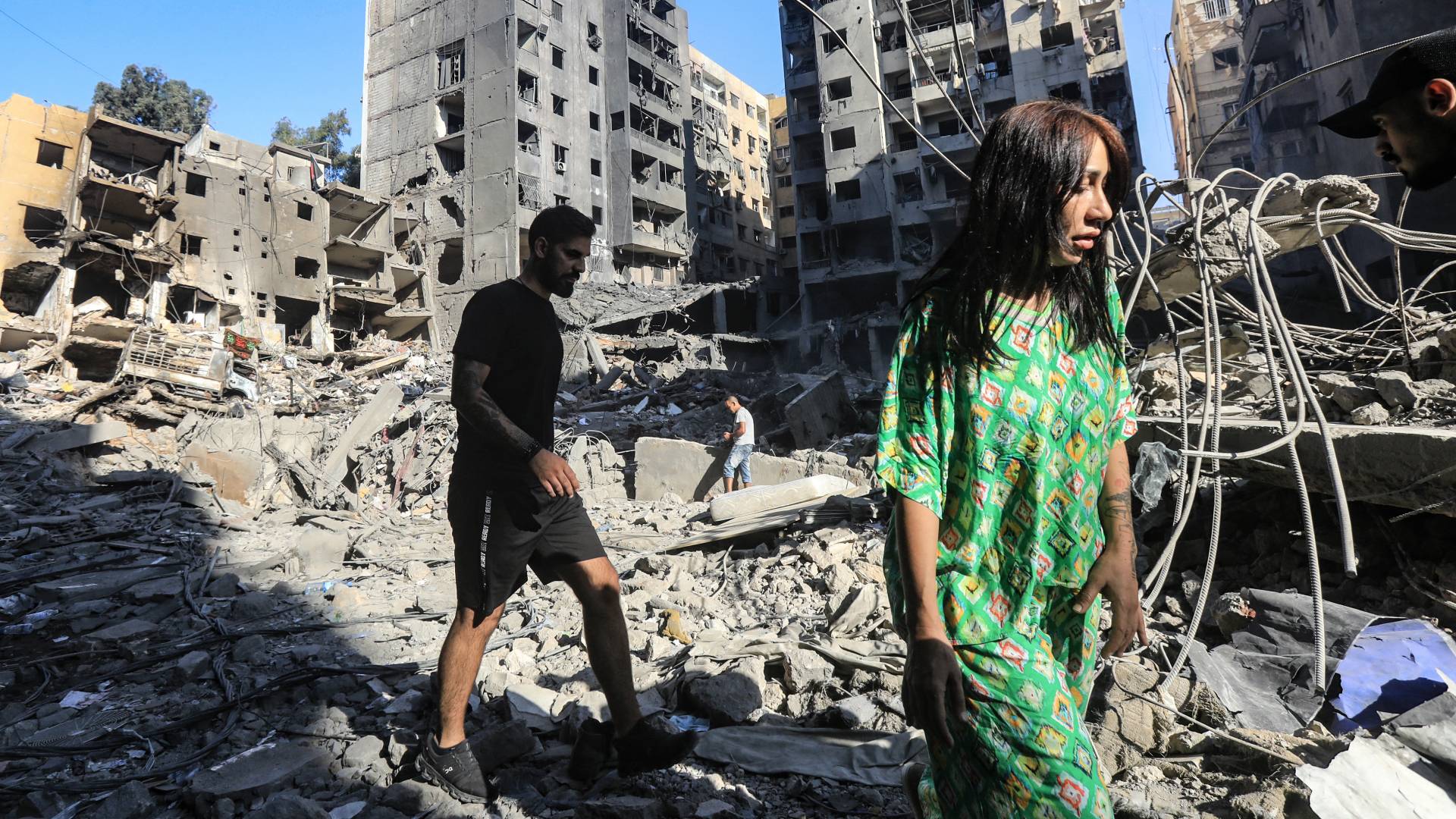 لبنانيون يسيرون وسط أنقاض المباني التي دمرتها غارات الاحتلال على الضاحية الجنوبية لبيروت.