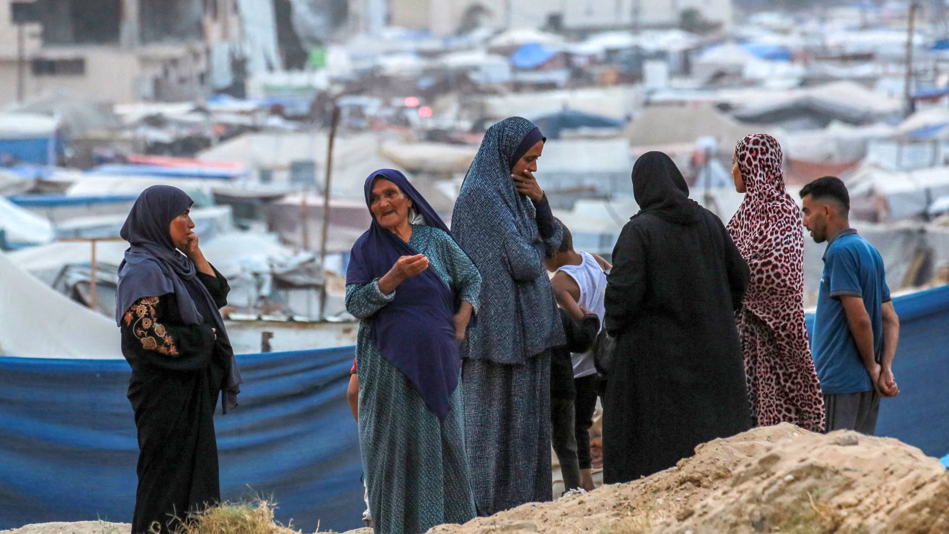 أشخاص يقفون على قمة تلة بالقرب من خيام تؤوي الفلسطينيين النازحين في خان يونس بجنوب قطاع غزة