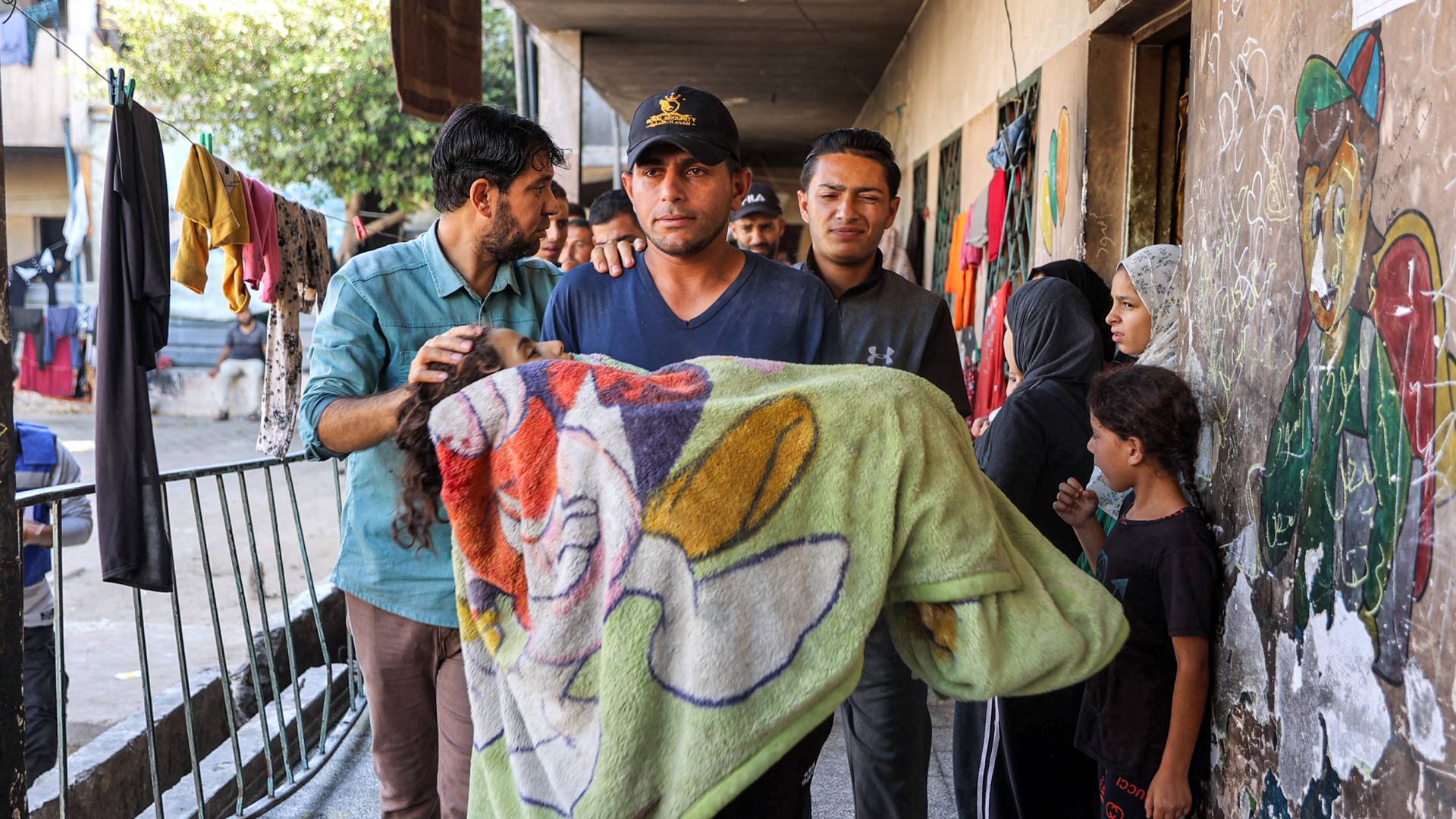 فلسطيني يحمل جثمان فتاة استشهدت في قصف على مدرسة الرافعي بمخيم جباليا