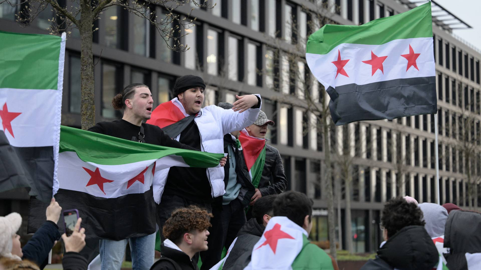 شباب يلوحون بأعلام علم المعارضة السورية أثناء تظاهرهم من أجل الحرية أمام محطة دويسبورغ غربي ألمانيا