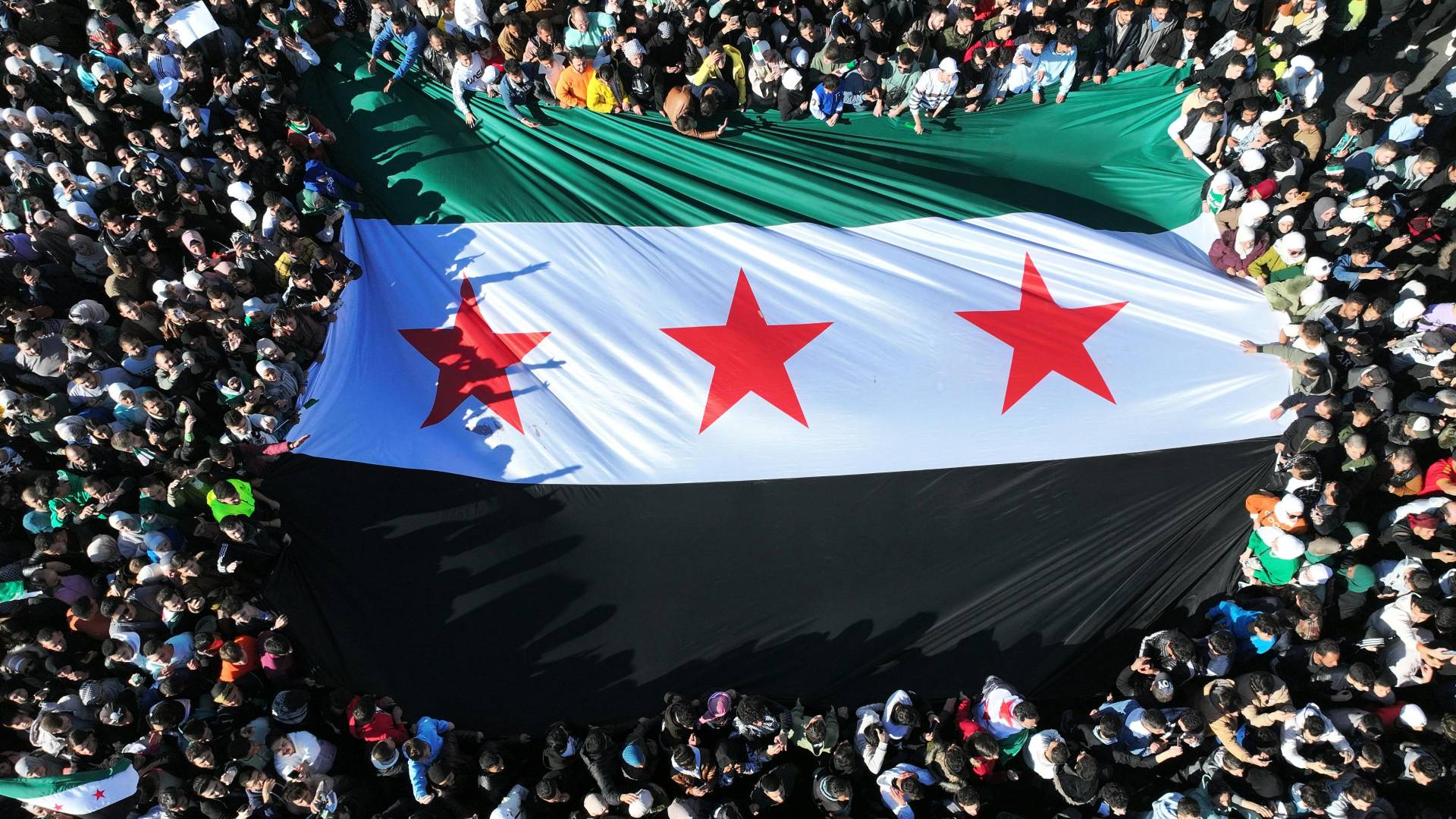 سوريون يرفعون علم الثورة السورية أثناء احتفالهم بسقوط نظام بشار الأسد