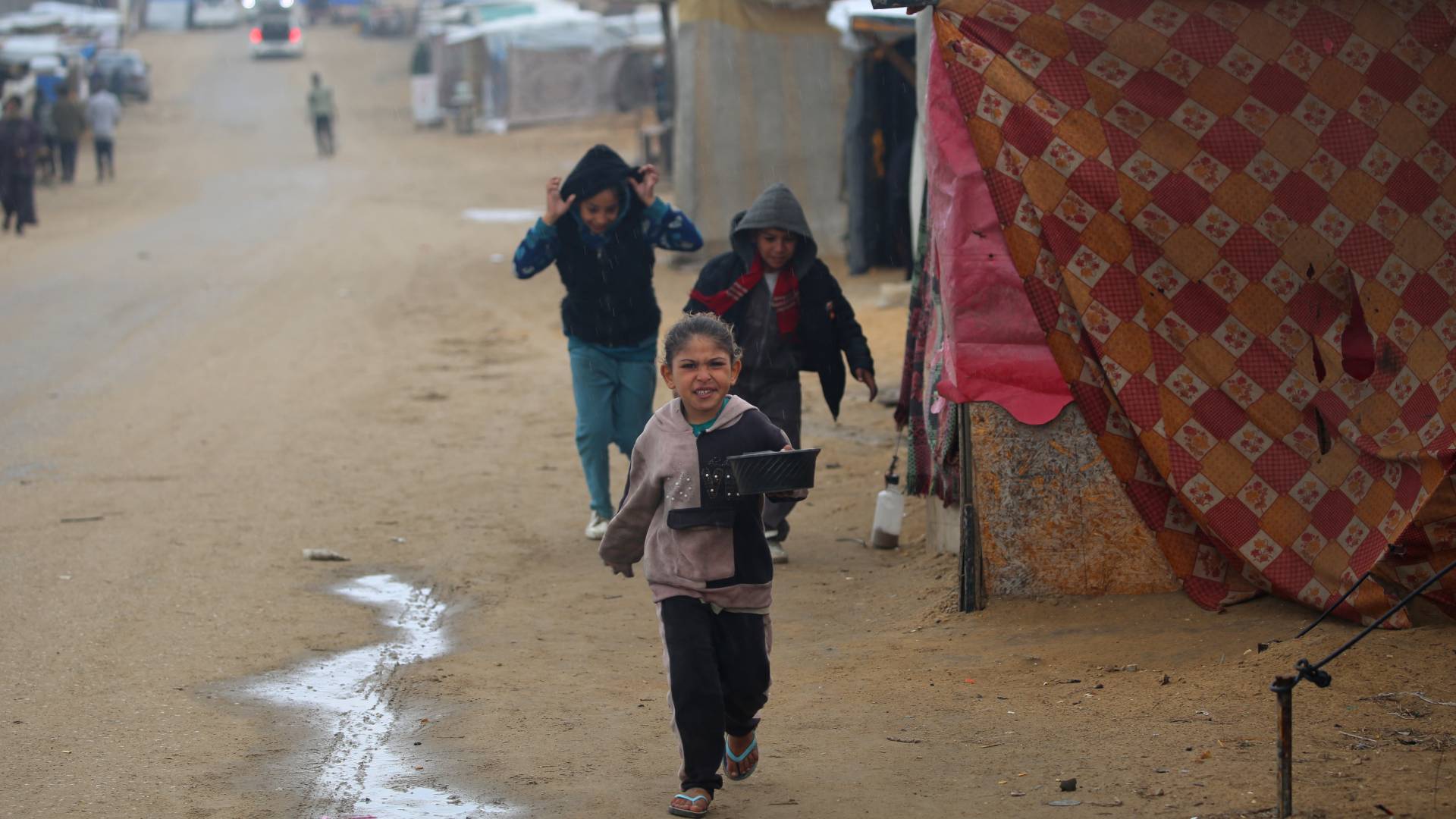 أطفال فلسطينيون يركضون للاحتماء من المطر في مخيم للنازحين داخليا على الشاطئ بالقرب من مخيم النصيرات للاجئين في وسط قطاع غزة