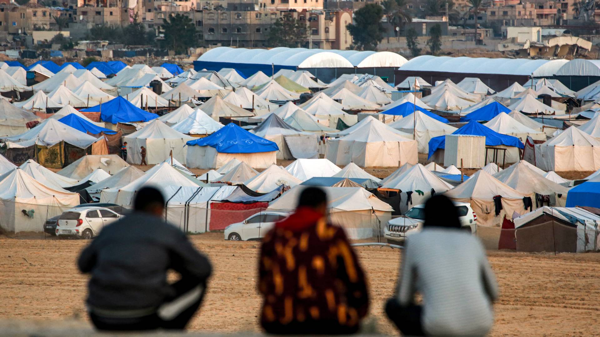 رجال يجلسون معا ويطلون على منظر الخيام التي تؤوي الفلسطينيين الذين نزحوا شمال خان يونس