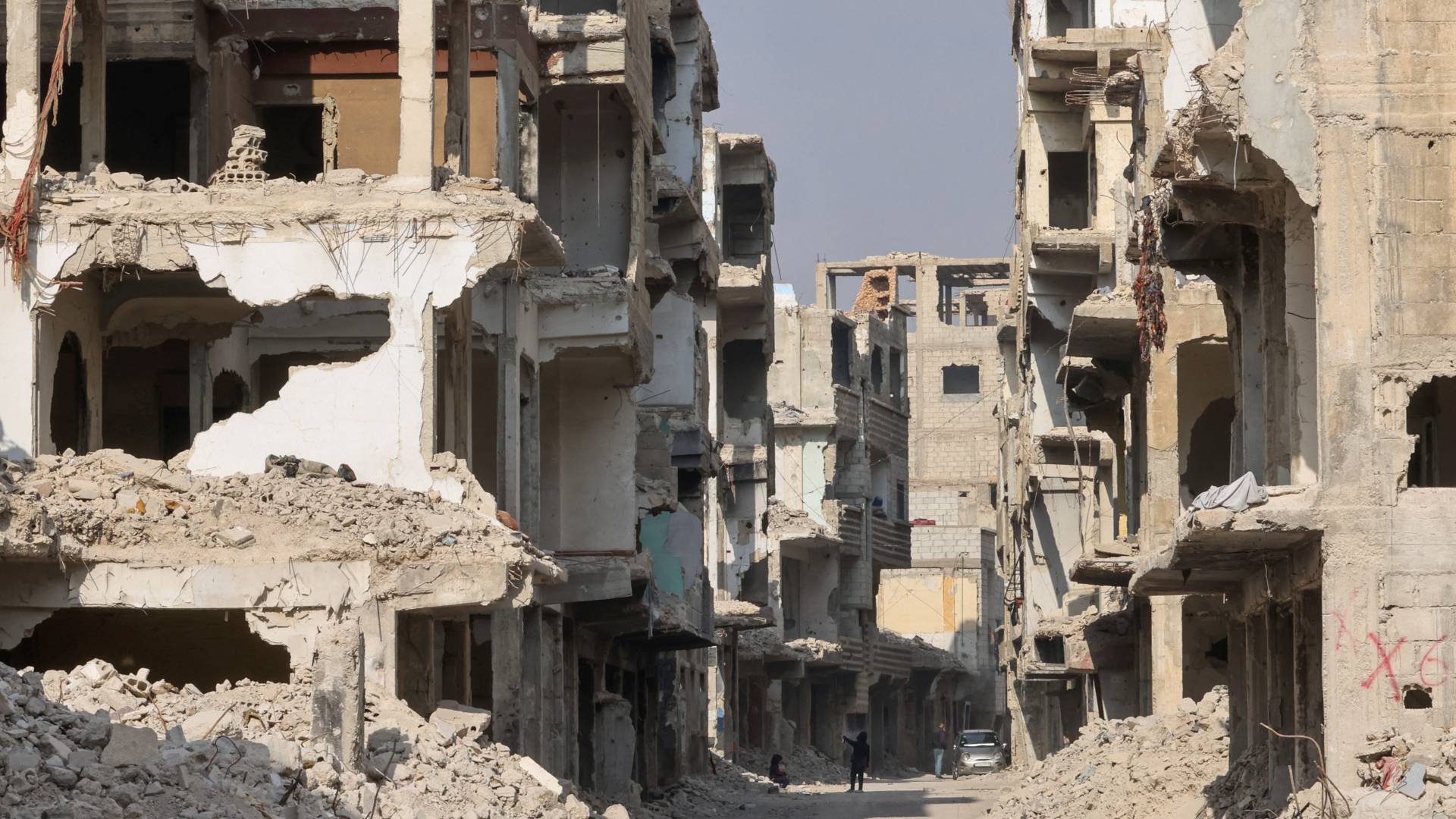 يجلس الناس في شارع تصطف على جانبيه المباني المتضررة بشدة في منطقة الحجر الأسود بالقرب من مخيم اليرموك في الضواحي الجنوبية لدمشق