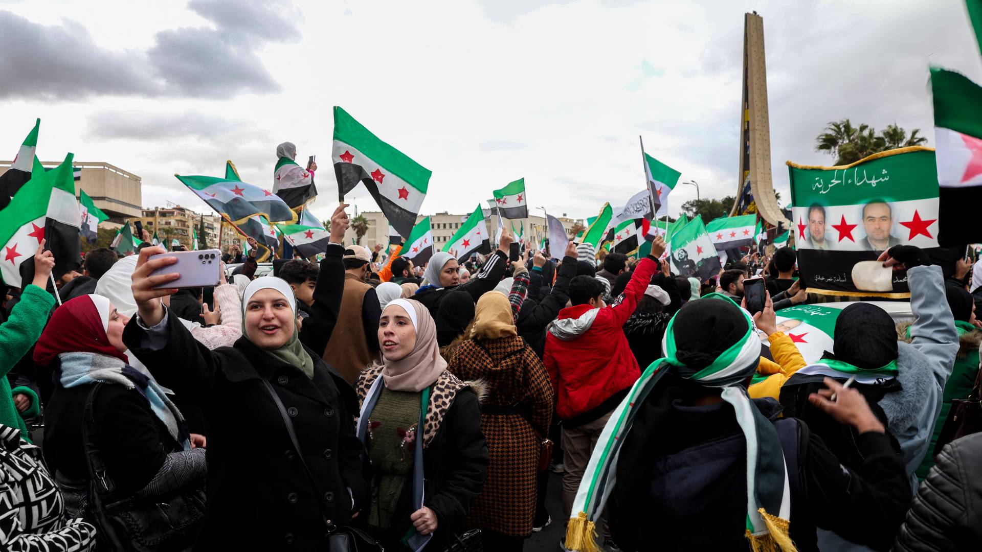 امرأة تلتقط صورة سيلفي بينما يلوح الناس بأعلام سورية من عصر الاستقلال خلال مظاهرة للاحتفال بسقوط الرئيس السوري بشار الأسد