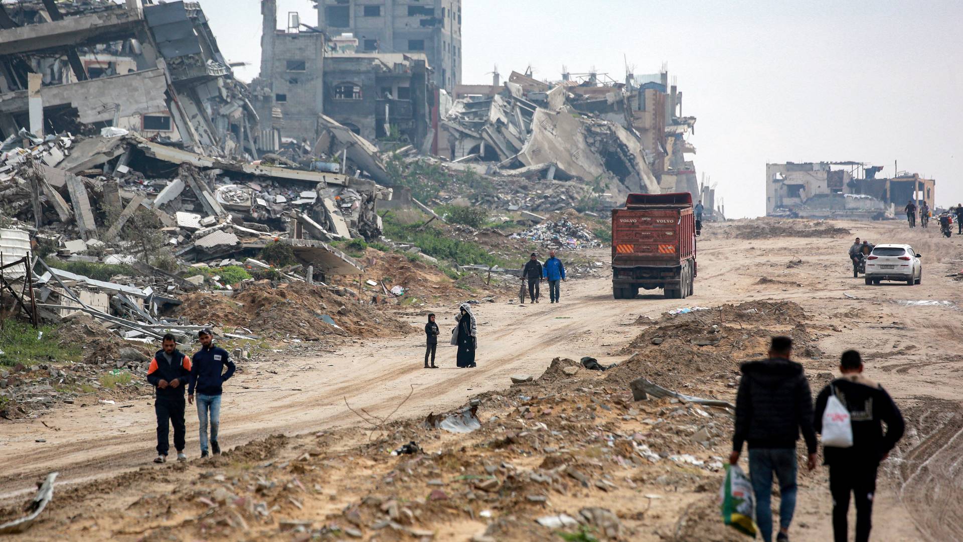 أشخاص يسيرون ومركبات تتحرك على طول طريق مدمر بجوار المباني المنهارة في غرب بيت لاهيا بقطاع غزة