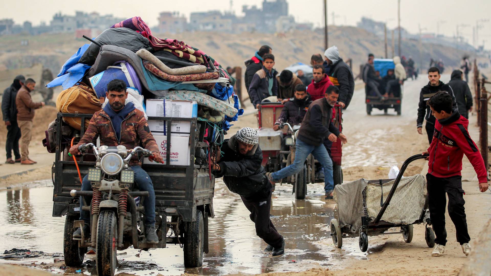 رجل يدفع عربة ثلاثية العجلات محملة بمراتب وممتلكات أخرى عبر جزء غارق من جسر وادي غزة