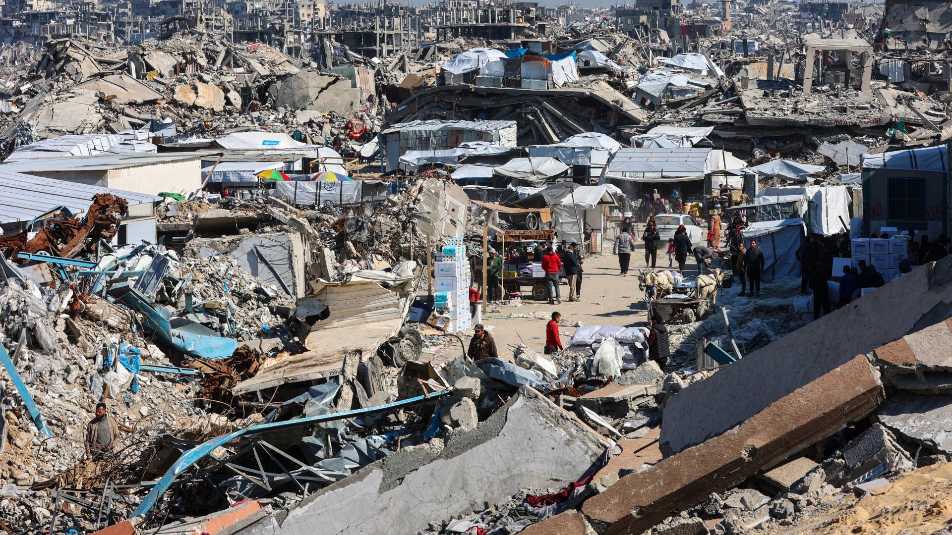 فلسطينيون يسيرون في سوق بجوار أنقاض المباني المدمرة في جباليا