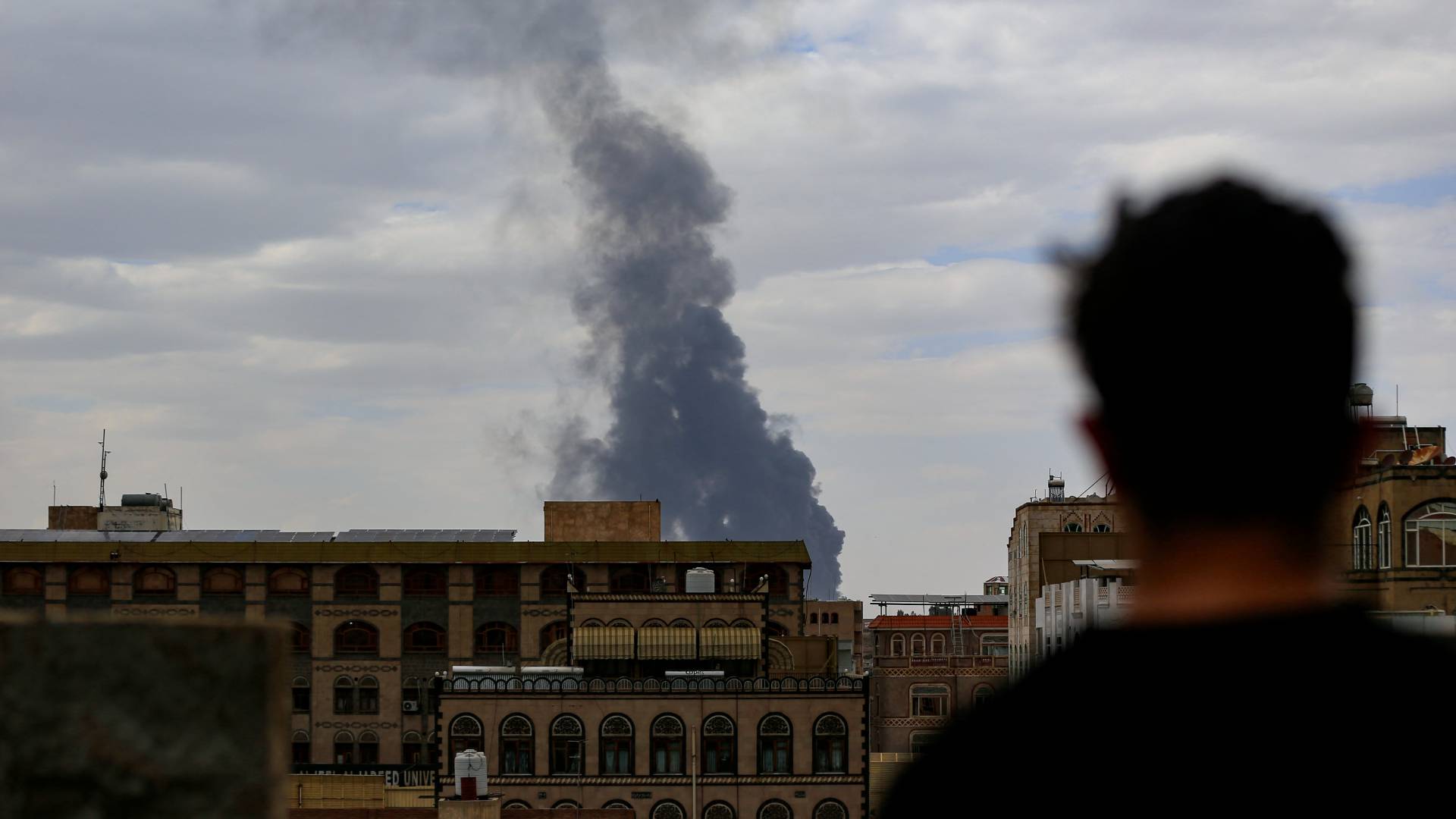 رجل ينظر إلى تصاعد الدخان في الأفق إثر غارة جوية إسرائيلية على العاصمة اليمنية صنعاء