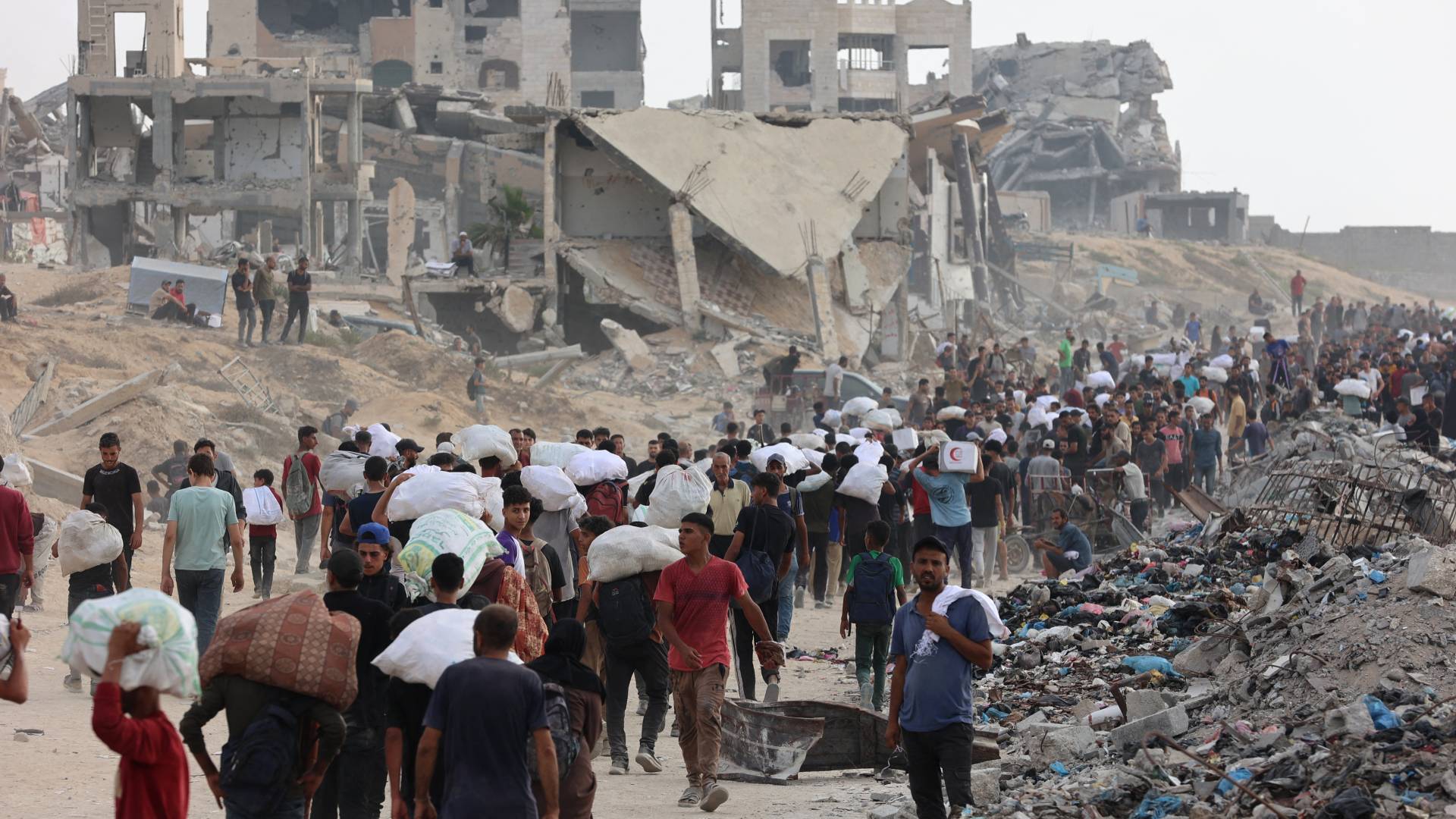 فلسطينيون يحملون مساعدات يسيرون على طول شارع الرشيد في غرب جباليا