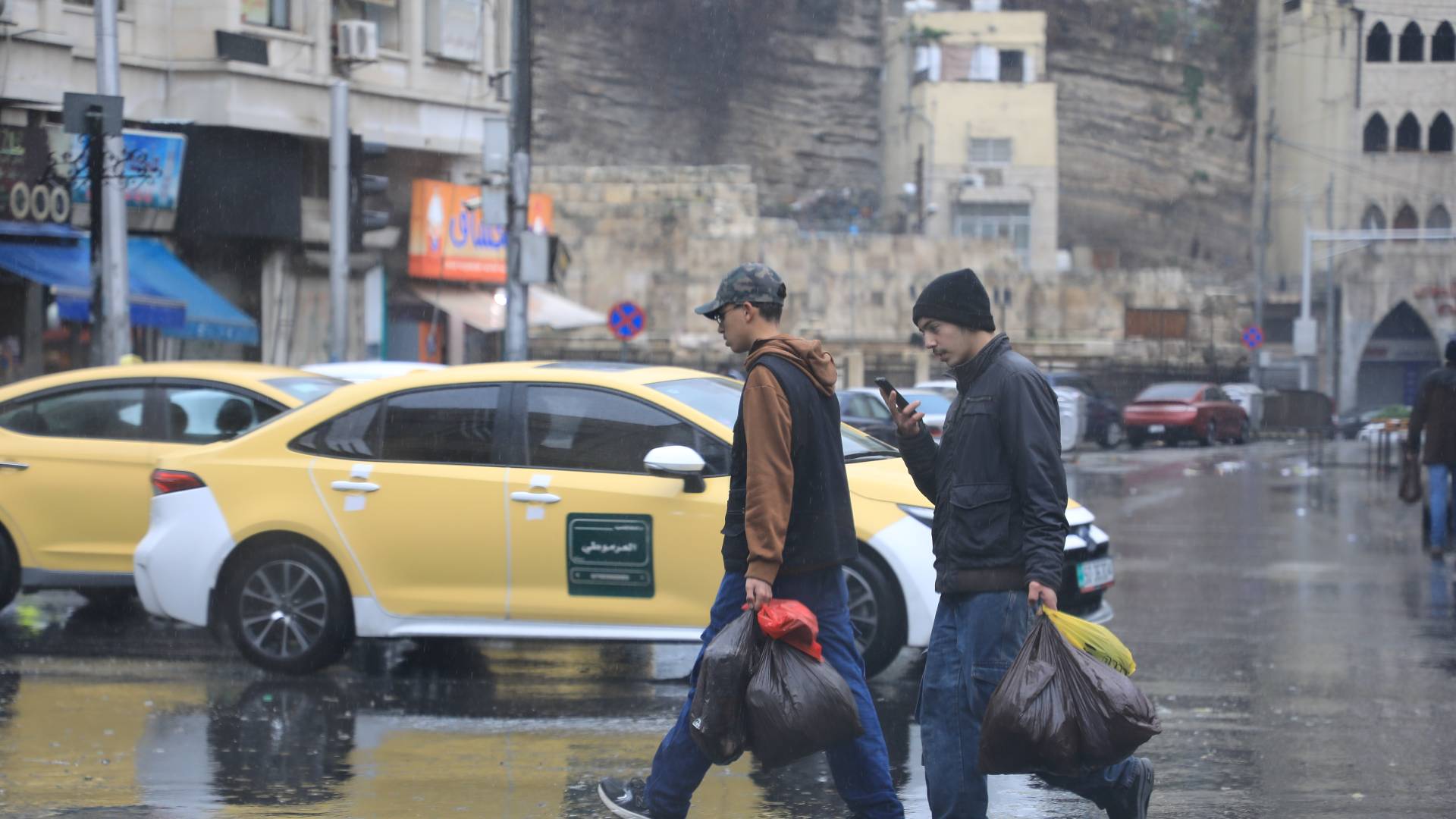 رجلان يسيران تحت المطر في العاصمة عمان