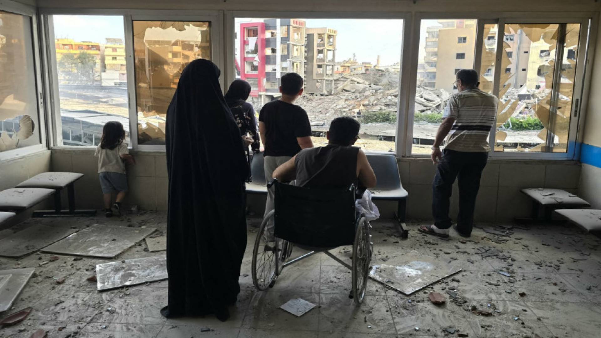 ينظر الناس من المستشفى المتضرر إلى موقع غارة الاحتلال وما خلفته