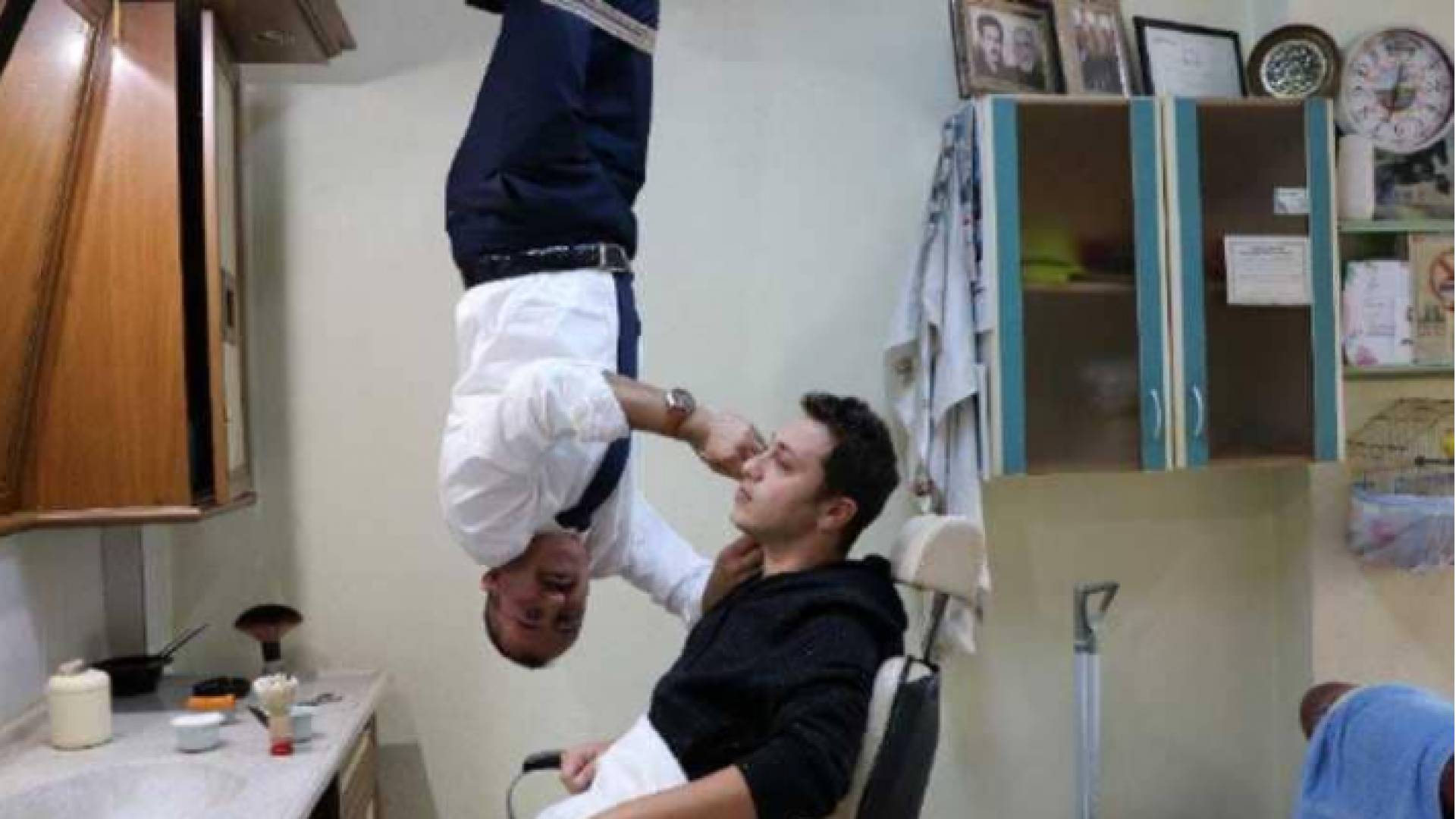 حلاق تركي يقوم بحلاقة ذقن زبائنه معلقا من سقف دكانه