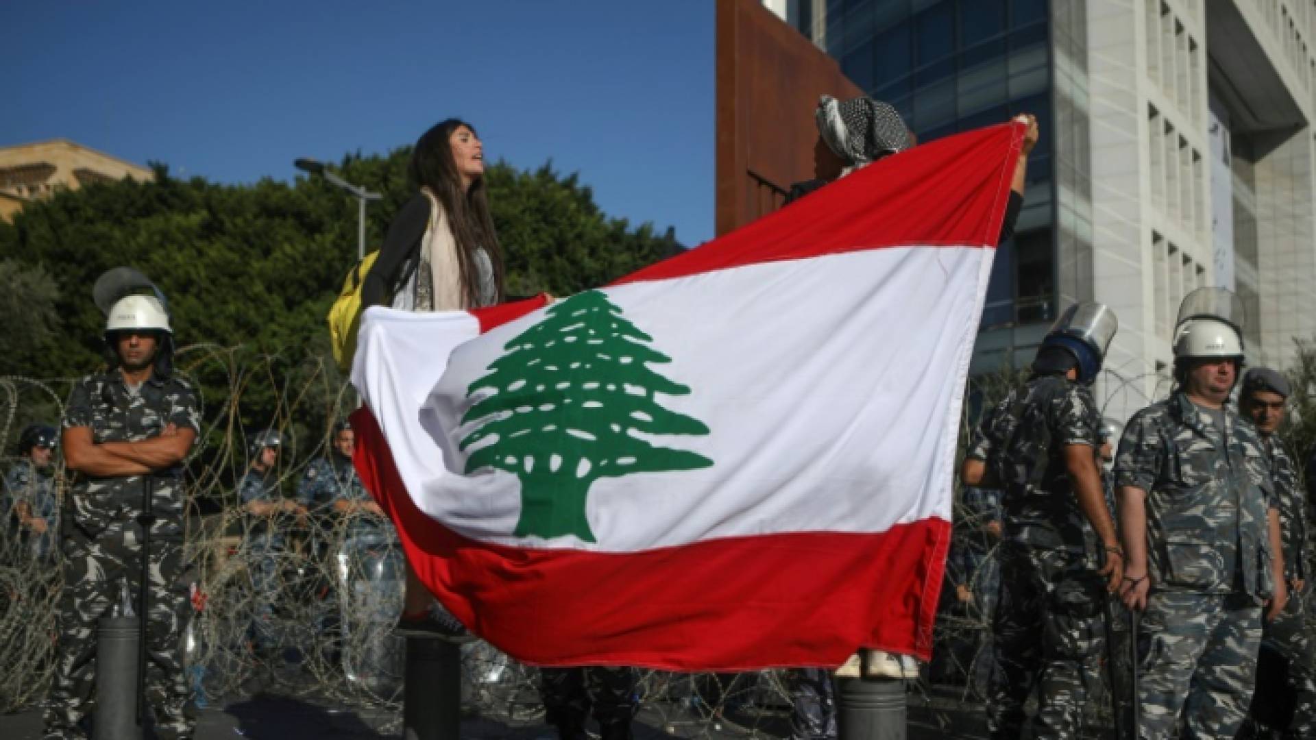 متظاهرتان ترفعان العلم اللبناني وخلفهما عناصر أمن قرب مقر البرلمان في وسط بيروت