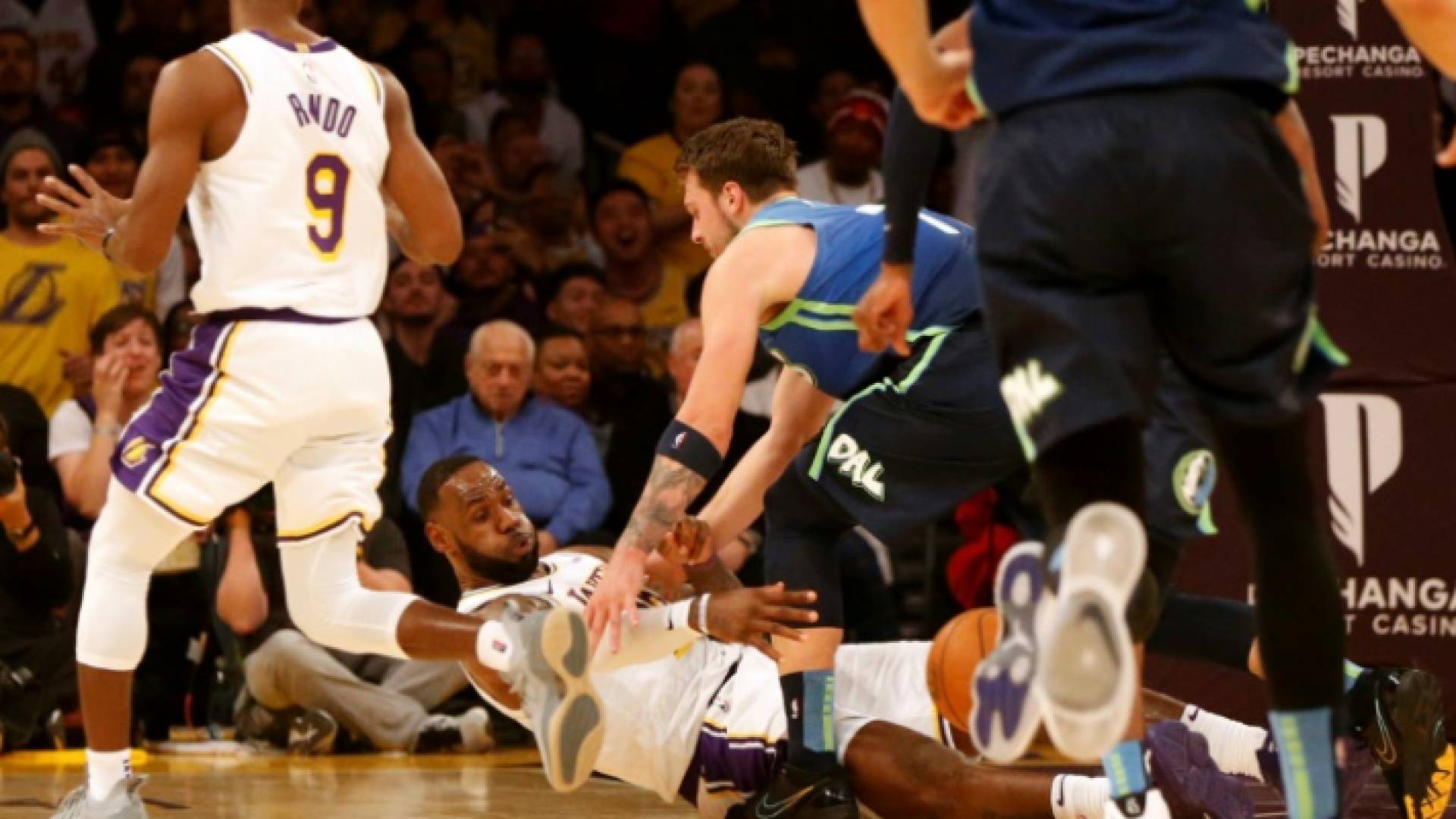 نجم لوس ألأنجليس ليكرز ليبرون جيمس (وسط) يمرر كرة بين ساقي نجم دالاس مافريكس السلوفيني لوكا دونسيتش