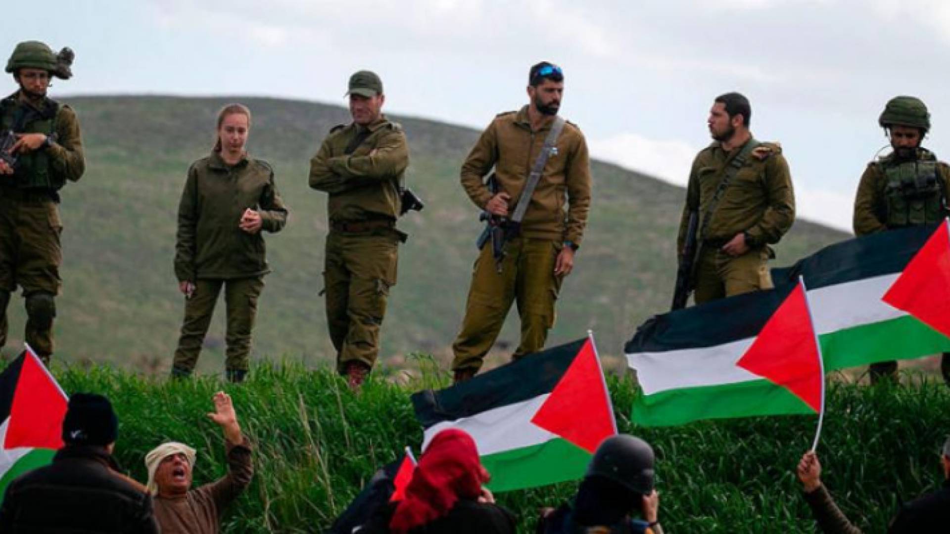 فلسطينيون محتجون ويرفعون العلم الفلسطيني في وجه جنود الاحتلال الإسرائيلي