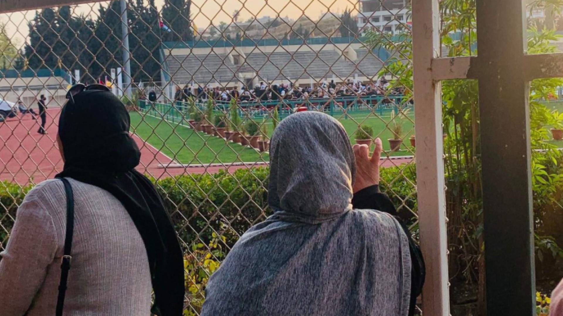 سيدة تتابع حفل تخريج أبنها من خلف أسوار الجامعة