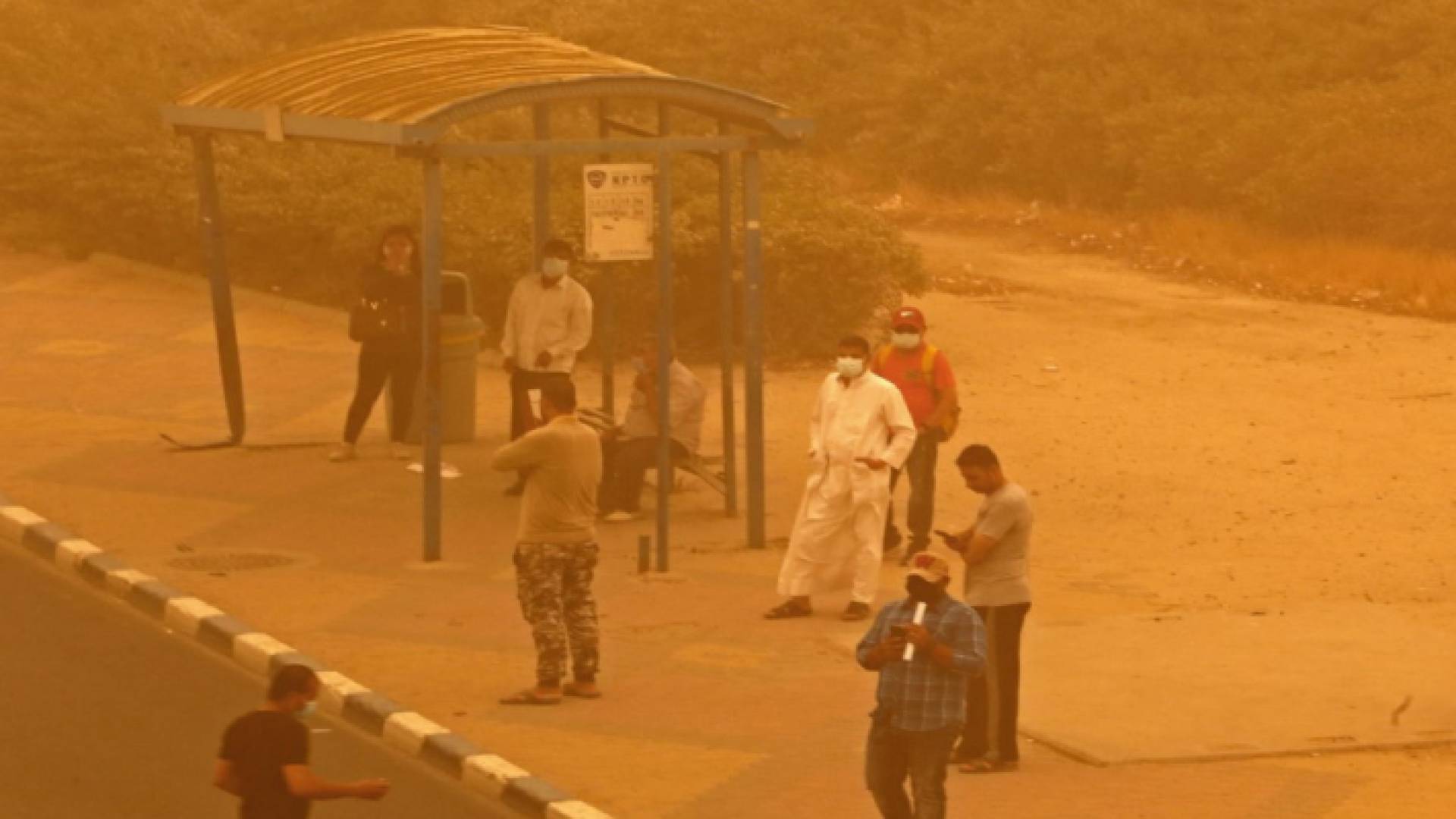 أشخاص ينتظرون في محطة للحافلات وسط عاصفة رملية شديدة في مدينة الكويت
