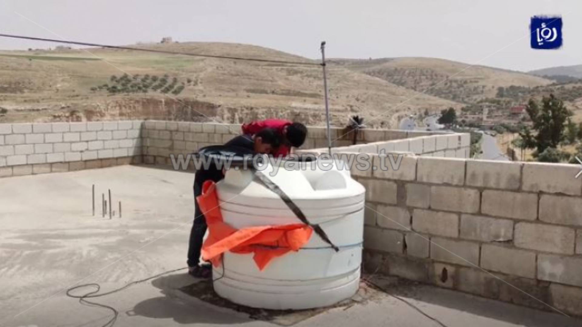 طفلان ينتظران وصول المياه إلى خزان فوق سطح بيتهم في حي أسد بكفرخل