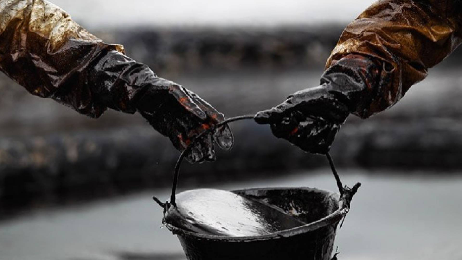 عاملان في منشاة نفطية يحملان دلوا من النفط - تعبيرية