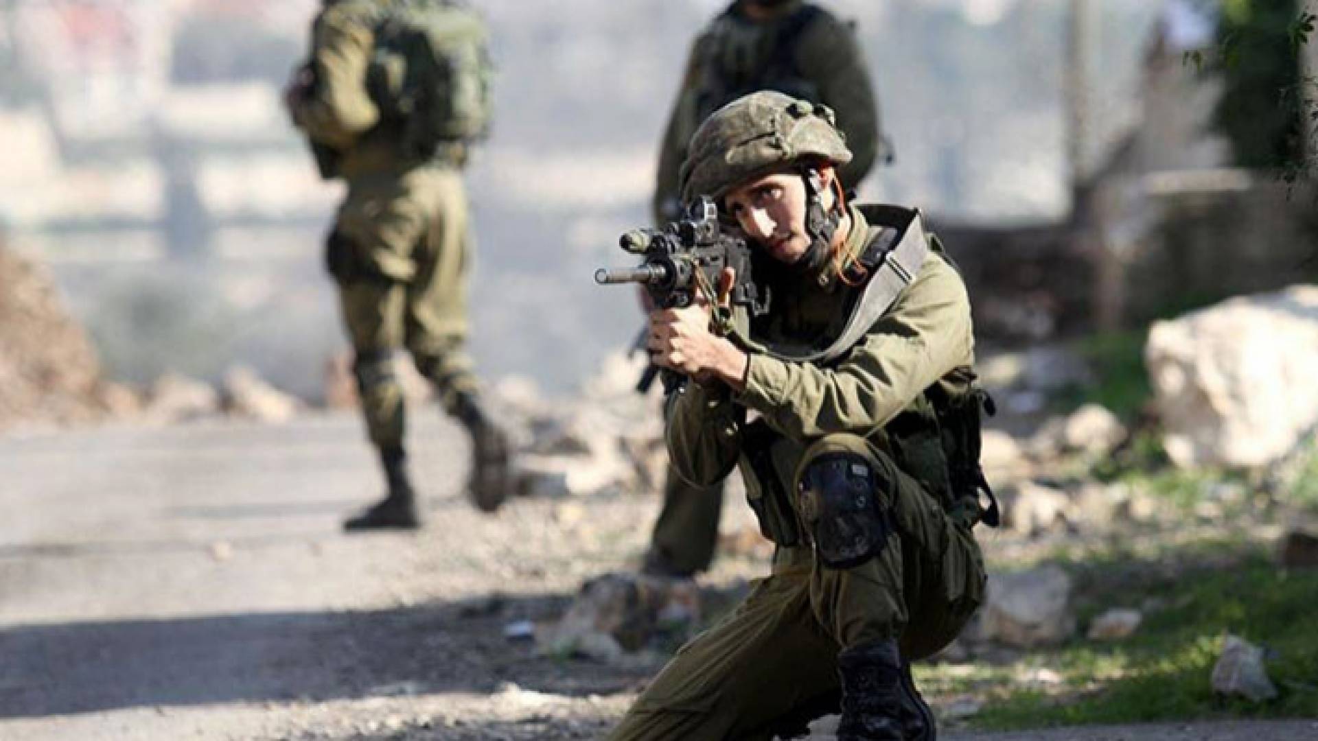 جندي إسرائيلي متأهب لتوجيه رصاص بندقيته نحو فلسطينيين