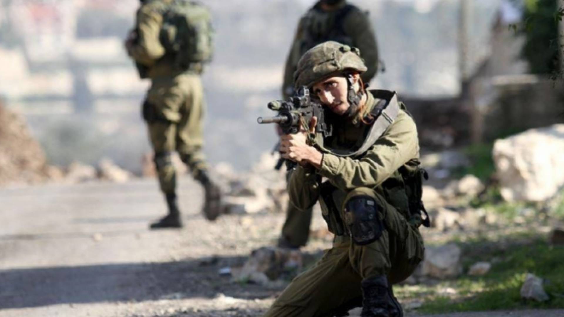 جندي من قوات الاحتلال يصوب بندقيته نحو فلسطينيين