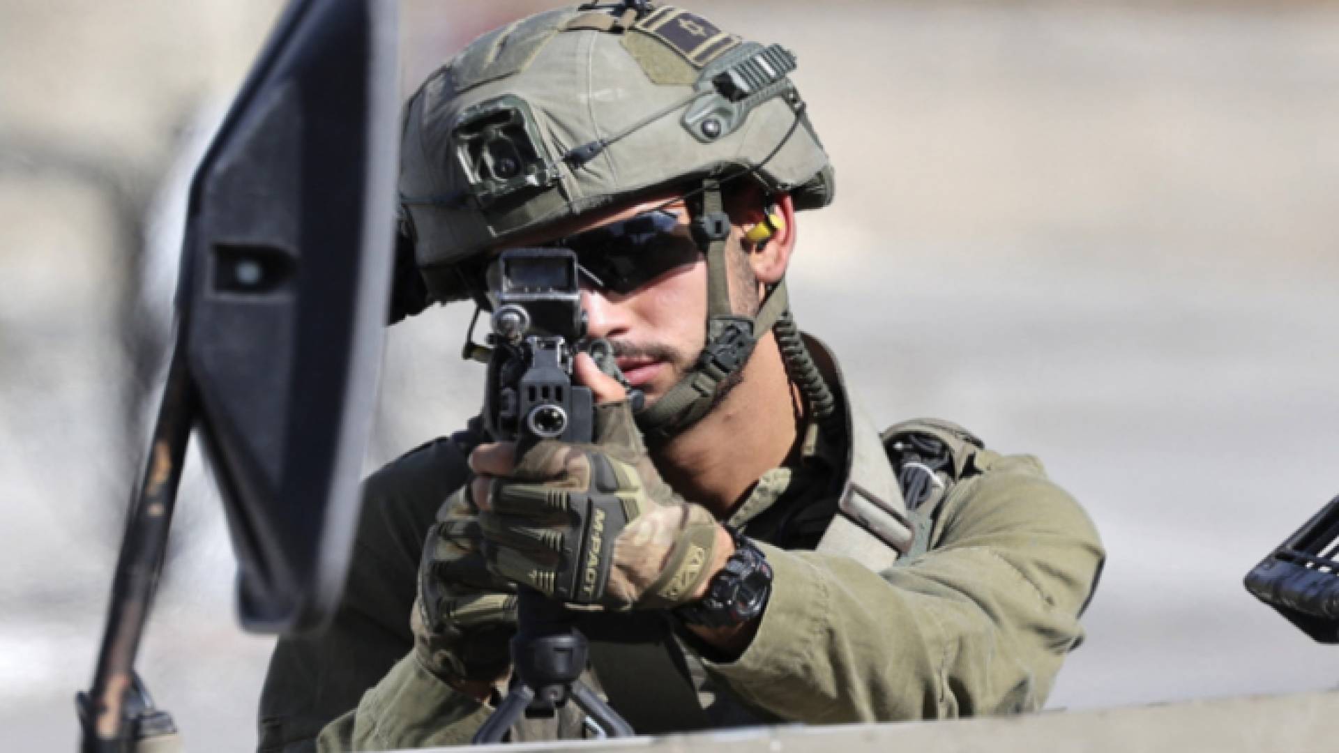 جندي في جيش الاحتلال يصوب بندقيته نحو فلسطينيين