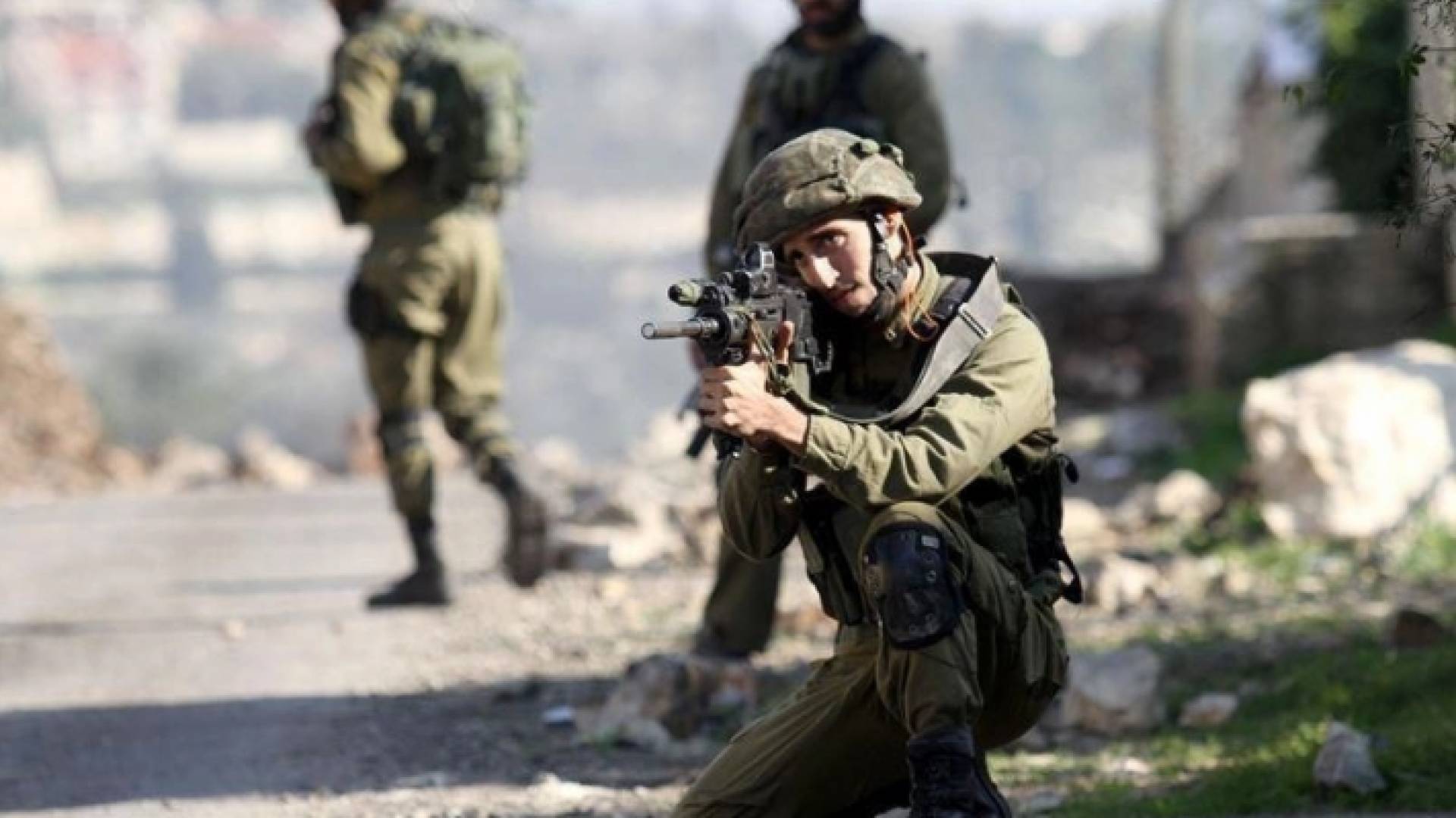 جندي من قوات الاحتلال يصوب بندقيته نحو فلسطينيين