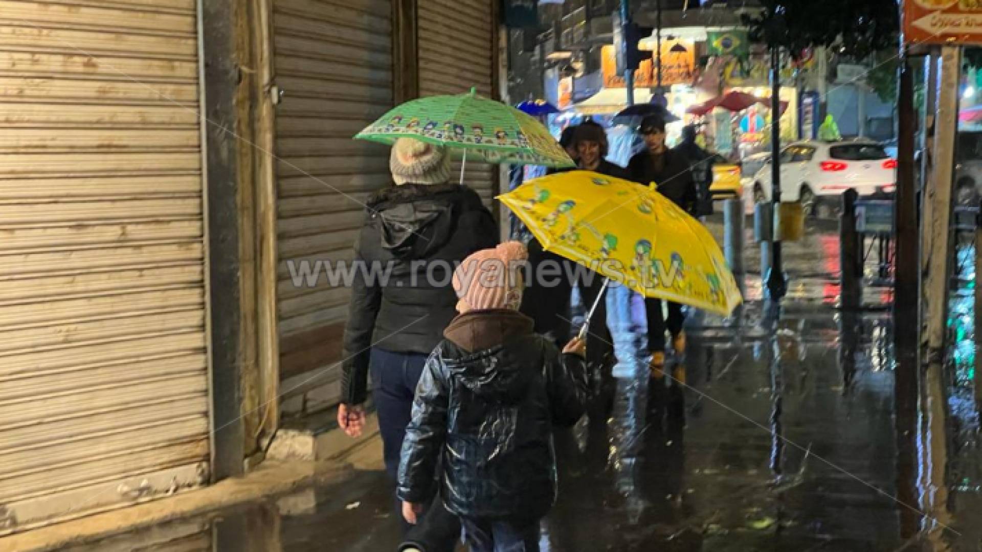 أشخاص يتجولون في أحد شوارع العاصمة عمان أثناء هطول الأمطار