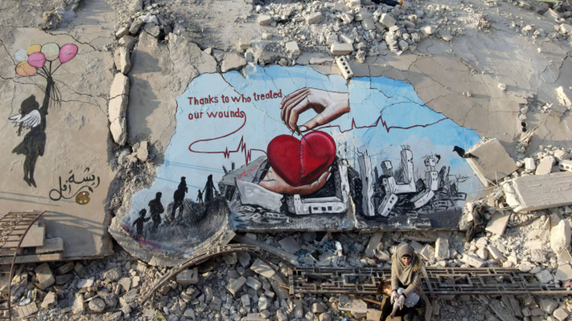 سيدة تجلس بجانب عمل فني مرسوم على أنقاض مبنى انهار خلال الزلزال