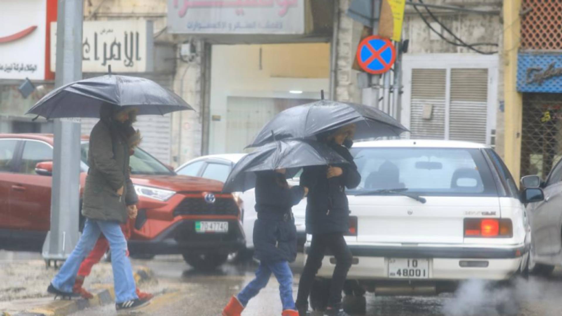 أشخاص يحملون مظلة في أحد شوارع العاصمة عمان