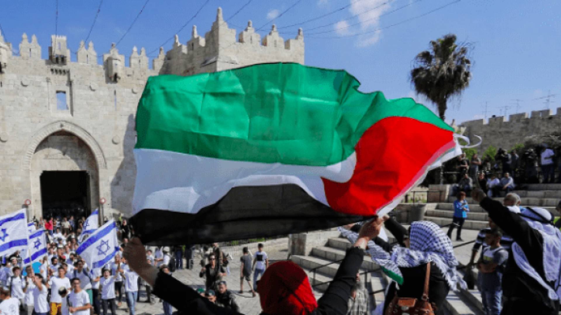 صورة مؤرشفة لفلسطينيون يحملون الأعلام الفلسطينية بوجه مسيرة الأعلام
