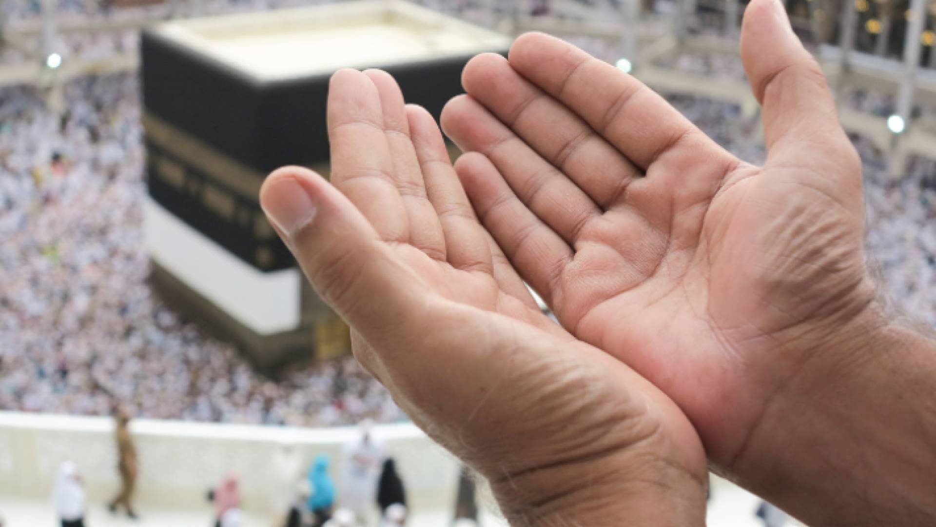 شخص يرفع يديه تضرعا إلى الله أمام الكعبة المشرفة