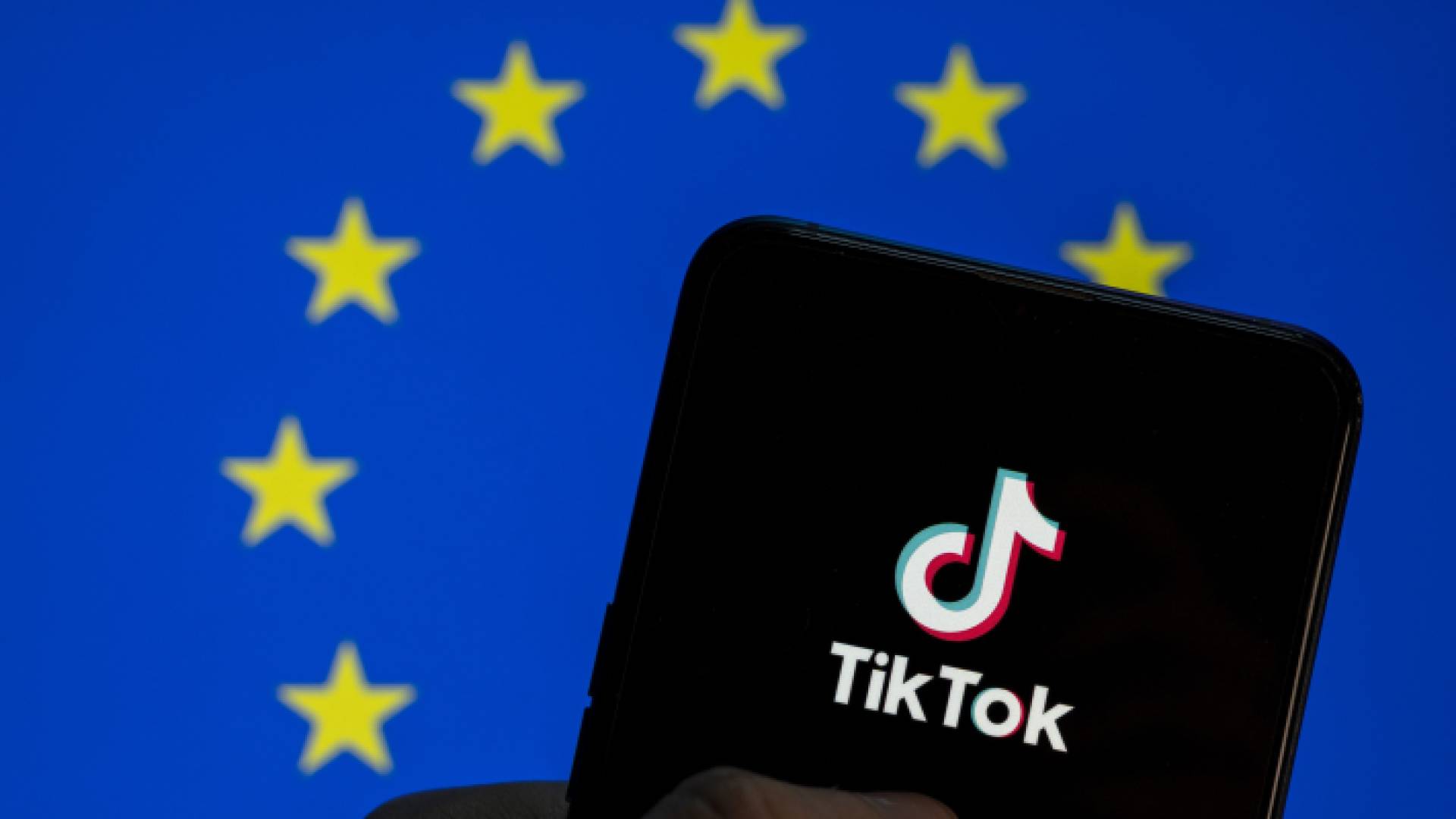 شخص يحمل هاتف ويتابع تطبيق تيكتوك وخلفه علم الاتحاد الأوروبي "تعبيرية"
